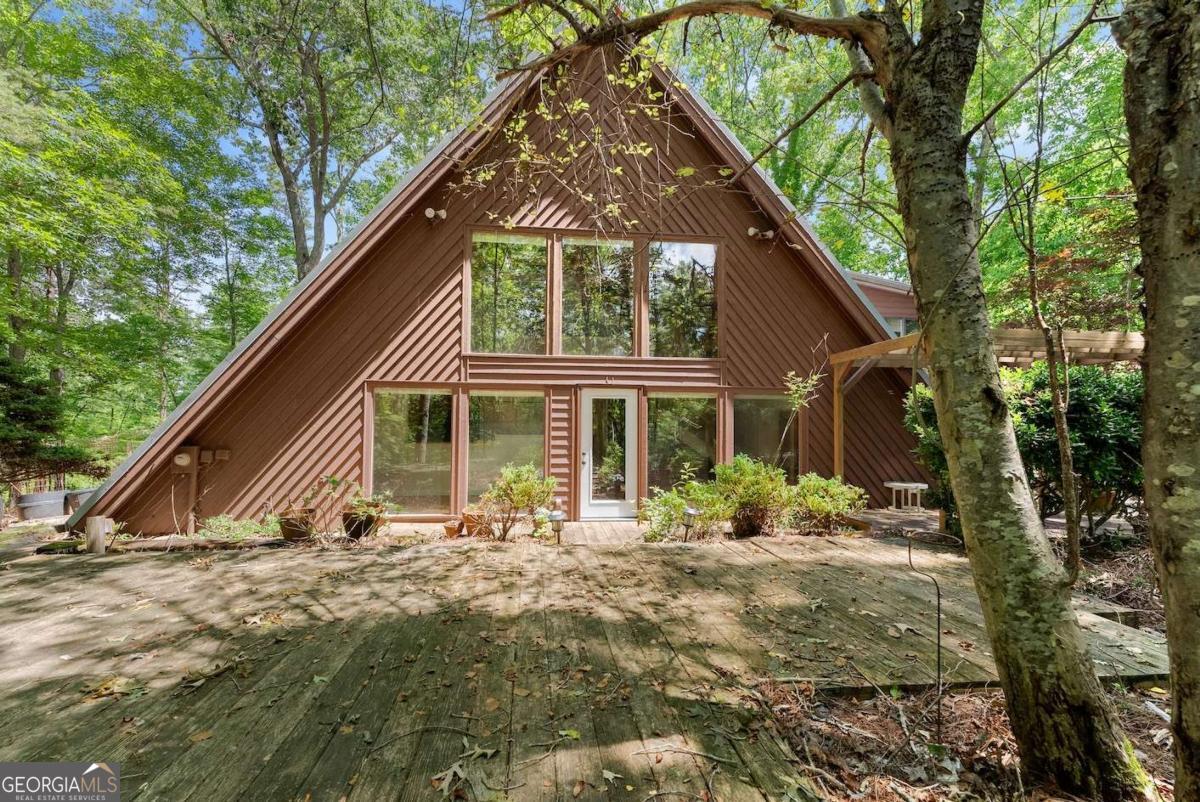 A hidden gem awaits on nearly 5.5 acres of pure serenity with more than 200 feet of Chestatee River frontage. A rare opportunity to own your own private escape in the foothills of the North Georgia Mountains. With a little TLC, this one-of-a-kind property is bursting with potential, whether you're looking for an investment, a peaceful getaway, or a forever home surrounded by nature. A built-in generator offers peace of mind, ensuring comfort and security no matter the season or weather. From the moment you enter, you're greeted by a breathtaking vaulted great room with soaring beamed pine ceilings, a wall of windows that floods the space with natural light, and a stunning contrast of stacked stone framing the original wood-burning stove. The adjoining kitchen is full of charm, featuring custom matching pine cabinetry that complements the natural warmth of the home. The main level also offers two bedrooms, a full bathroom, and a storage room for added convenience. Upstairs, enjoy complete privacy in the primary suite with a double vanity, makeup counter, walk-in shower, elevated soaking tub, and generous closet space. A bonus room offers flexibility for an office, studio, or quiet retreat, while a large upper deck overlooks your own secluded slice of paradise. The screened-in patio complete with a hot tub, the perfect place to unwind year-round. A separate storage shed provides ample space for equipment, tools, or even a future workshop. Stroll down to the riverbank for a day of fishing or simply relax to the soothing sounds of flowing water. Located near award-winning vineyards and wineries like Cavender Creek Vineyard, and surrounded by seasonal events, fall festivals, charming shops, and local dining, this property is a true retreat with endless possibilities to customize, enjoy, and make your own. ESTATE OWNED HOME. STR ALLOWED. PLEASE NOTE THIS HOME IS FAR OFF THE ROAD. GRAVEL/ DIRT ROADS. DUE TO STORMS THIS WEEK, TREES ARE DOWN AROUND HOME. EXPECTING OFFERS AND WILL ACCEPT THROUGH SUNDAY 8PM.