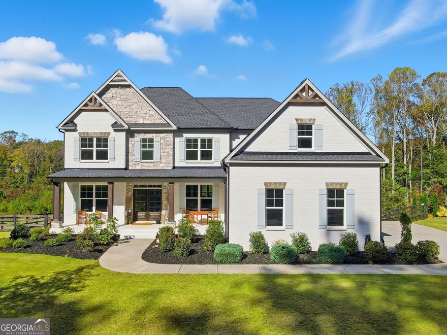 Set within the sought-after Milton Overlook community near Birmingham and Batesville Road, this home combines high-end design with everyday comfort. The exterior blends painted brick and stone for timeless curb appeal, while the inviting front porch hints at the open, light-filled interiors inside. Step into the two-story great room where a wall of soaring windows and a sleek fireplace frame serene, protected green space-no neighbors behind you, just a backdrop of nature and sky. Each evening, the view transforms as the sun sets across the treetops, casting warm light into the room and painting the sky in color. The open layout flows effortlessly into the chef's kitchen, complete with white craftsman cabinetry, a massive quartz island, stainless-steel appliances, a gas cooktop, and a double oven for effortless entertaining. A butler's pantry and drop zone help keep life organized, while 10-foot ceilings elevate the dining and library spaces. The main-level guest suite offers privacy and natural light, perfect for visitors or multi-generational living. Upstairs, the oversized primary suite features a sitting area and an expansive custom closet. The spa-style bath invites relaxation with a freestanding soaking tub, walk-in shower, and dual vanities. Three additional bedrooms each include large closets and access to well-appointed baths. The unfinished daylight basement with tall ceilings and full-size windows offers space to expand with a theater, gym, or recreation room. Outdoors, enjoy  terrace level patio and deck overlooking a fenced yard and forever-green views-perfect for morning coffee or sunset evenings by the fire pit. Additional features include a three-car garage with an electric-vehicle charging port, and community amenities such as a pool, tennis courts, and a playground.