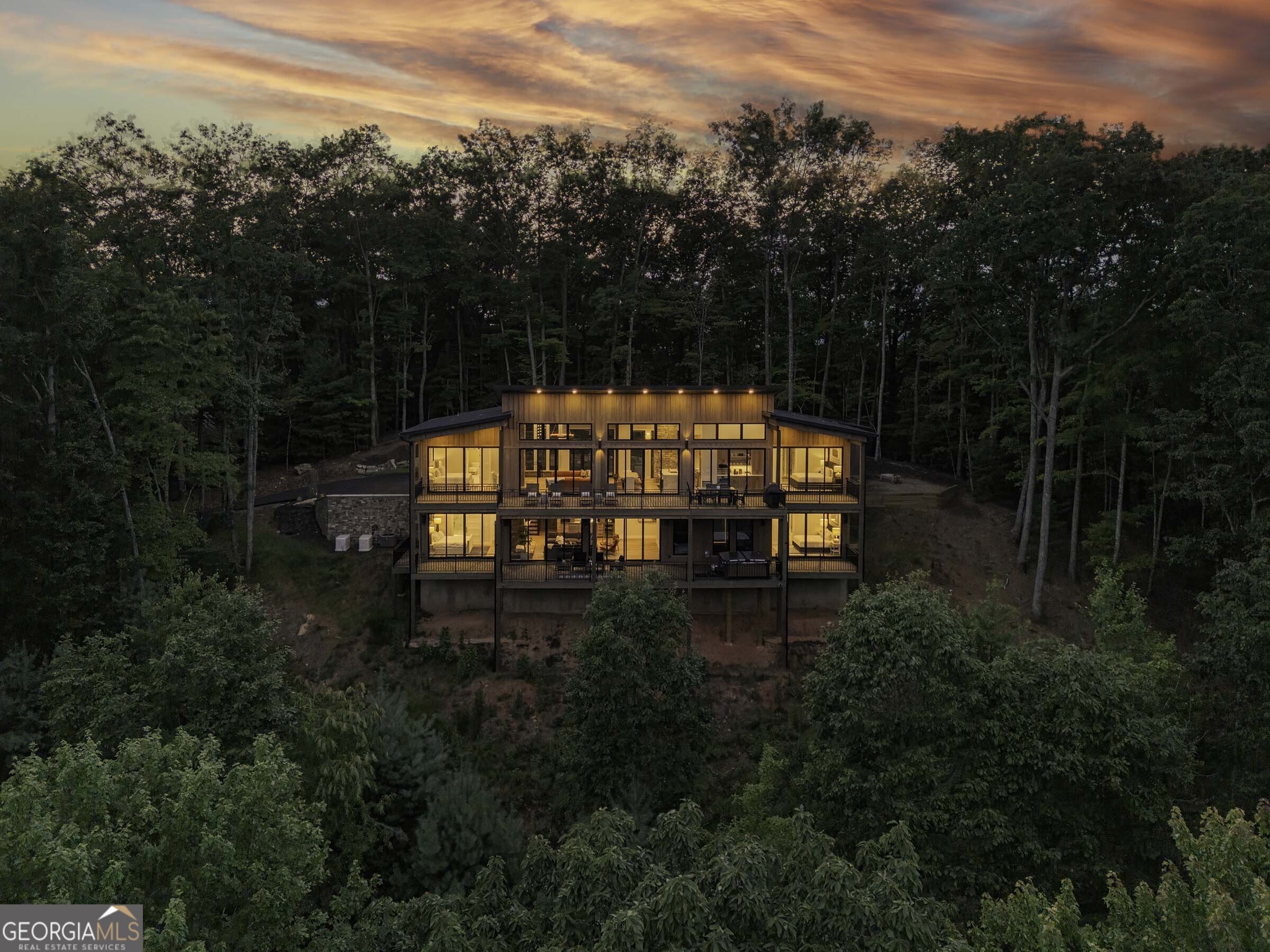 Seamlessly blending contemporary elegance with the timeless rustic warmth of a true mountain chalet, The Lodge at Little Creek Overlook beckons for a redefined luxury mountain lifestyle one of its kind. Tennessee field stone, cypress wood siding and rolled steel blend harmoniously with walls of glass as you're greeted with the front facade of the home. Gaze through the front door and see through the home and out towards the layered mountain views and panoramic scenery atop the mountain. Backing up to acres of USNF land, this home is completely private and tucked away. On the interior, find it complete with five bedroom suites and two powder rooms. The main level is a stunning open-concept with a large living room accented by a custom masonry stone and steel fireplace. Dining and kitchen make for the perfect entertainer's home. Sliders off the living, dining and even butler's pantry from the kitchen open the outdoors and invite the mountains inside. Find the gourmet kitchen adorned with custom cabinetry and quartz countertops with waterfall edges. Home is fully equipped and stocked for the chef at heart. Main level has a large laundry room, a powder room, two primary suites, and a wing leading to the fully-finished two car garage. Main level deck is built with TREX decking and steel railings. On the terrace level, find a large den area with fireplace, full bar, three additional bedroom suites, bountiful storage and utility areas. Walk-out terrace deck is set up with a jacuzzi overlooking the lush mountain scenery. Home has been equipped with two generators, two buried propane tanks, a TESLA charger, and sold fully furnished! Located in the highly sought-after Aska Adventure Area and minutes from the Toccoa River, Lake Blue Ridge, and the best hiking and biking trails all while gated w/ all paved access. The fine details of this home are at length -- reach out for more information. Discover the contemporary mountain lifestyle today!