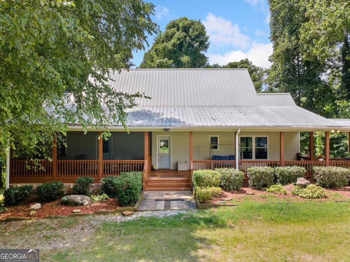Nestled on just over 3 acres surrounded by Ellijay's iconic apple orchards and natural beauty, this picturesque property offers the perfect blend of peaceful country living and versatile space. The spacious farmhouse features low-maintenance vinyl siding, a durable metal roof, and abundant outdoor living with multiple covered porches and a screened-in porch, ideal for savoring the serene surroundings. Step inside to a warm and welcoming open floor plan with a stylish mix of drywall and tongue-and-groove ceilings that create a rustic yet airy and bright feel. The kitchen has a large angled island with bar seating, ample cabinetry and counter space, stainless steel appliances, and an adjacent dining area. The vaulted-ceiling great room is a spacious spot perfect for gathering and centers around a cozy wood-burning fireplace. The main-level master suite is impressively sized and includes a bonus flex space ideal for an office, reading nook, or exercise area and leads into an ensuite bath with a shower and large vanity. The main level also has a laundry area and convenient half bath. Upstairs, a generous second bedroom with vaulted ceilings and a connected half bath offers versatility for guests or as a beautiful private office suite. Downstairs, you'll find two additional large bedrooms, including one with an ensuite bath, plus a substantial mechanical/storage room. Take the covered breezeway to the deep, oversized detached garage with plenty of storage space. Attached is a complete, 720 sq/ft apartment that also has its own private entry, with a full kitchen, living & dining space with French doors to the outside, washer & dryer, a bedroom, and a full bath; this space is perfect for multi-generational living or has the potential for rental income. Fully fenced with a gated entrance and no restrictions, this property is ideal for beginning your farmstead with animals or for your own private retreat in the heart of North GA. Ready for you to make your dreams come true!