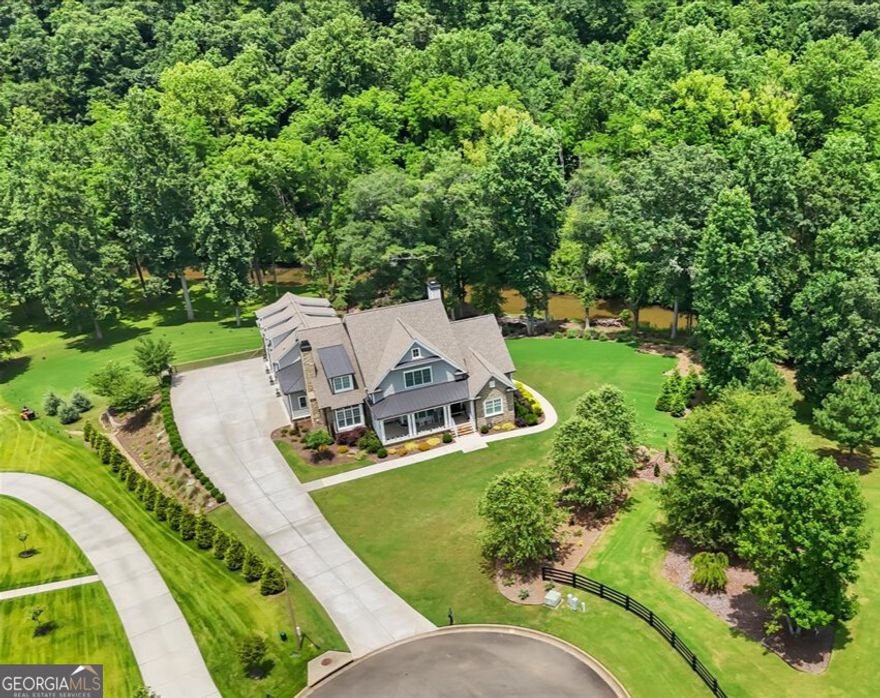 Experience the rare opportunity to own an extraordinary luxury estate, a tranquil masterpiece nestled on two private, park-like acres with stunning frontage on the serene Sharp Mountain Creek. This one-of-a-kind residence is the perfect fusion of natural beauty and refined living, offering an unforgettable setting where the soothing sound of flowing water and complete backyard privacy define the everyday. Tucked away in an exclusive cul-de-sac, this meticulously designed Craftsman-style home presents a sprawling floor plan with 5 spacious bedrooms, 5 full bathrooms, and 2 half baths, reflecting a commitment to luxury finishes throughout. Step inside to discover timeless elegance and elevated design. The main level features hardwood floors, an open concept layout, and detailed millwork. Walls of windows frame peaceful landscape views. The heart of the home is a chef's kitchen with custom cabinetry, upgraded GE Monogram appliances, quartz countertops, a large island, farmhouse sink, and a stunning wood-trimmed range hood. This space flows effortlessly into a vaulted keeping room with a stone fireplace, and a grand family room with a coffered ceiling and a second stone fireplace offers additional luxury living space. The main-level primary suite is a private sanctuary featuring a sitting room and a massive walk-in closet, complete with a spa-like ensuite offering quartz dual vanities, a soaking tub, and an elegant custom-tiled shower. The upper level hosts three thoughtfully designed bedrooms, each with its own ensuite bath, ensuring comfort and privacy. A separate staircase leads to an expansive bonus room, ideal for a home office or playroom. The fully finished terrace level provides a seamless extension of the home's living and entertaining space. It includes a second fully-equipped kitchen, an inviting media room, private guest quarters, a fitness room, and a beautifully appointed family room, perfect for sophisticated entertaining. The backyard is a masterpiece-a tranquil creekside retreat. Enjoy summer evenings gathered around the firepit, soaking in the hot tub, or relaxing on the screened porch-all while overlooking the creek and beautifully manicured grounds. Premium features include a whole-house generator with surge protection, tankless water heater, irrigation system, and a spacious 3-car garage. Located in a top-rated school district with convenient access to the interstate and minutes from the charming downtown Ball Ground. This is more than a home-it's a sanctuary where elegance, serenity, and modern luxury unite in perfect harmony. Schedule your private showing today to experience this unparalleled creekside lifestyle!