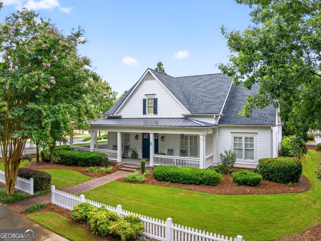 Welcome to this luxuriously upgraded 5-bedroom, 4-bathroom home in the highly sought-after Georgia Club, a gated golf course community known for its Southern charm and resort-style amenities. Situated on a premium corner lot, this beautifully maintained home features a white picket fence, a charming wraparound front porch, and a rear-entry garage, all adding to its curb appeal. Inside, enjoy new flooring, fresh interior and exterior paint, and thoughtful architectural details throughout. The spacious living room features a coffered ceiling, creating a sophisticated and inviting space for gatherings. The kitchen is accented with brick details, blending rustic warmth with modern utility. Perfect for remote work or study, the private office includes custom-built-in shelving. The oversized primary suite is a true retreat, featuring two large custom walk-in closets and a spa-inspired en suite bathroom with a large walk-in shower, double vanities, and elegant finishes. Enjoy year-round efficiency with a solar energy system and keep your landscaping lush with the automated sprinkler system. Located in The Georgia Club, residents have access to world-class amenities: golf, pools, tennis courts, clubhouse, fitness center, and walking trails. This home offers a rare combination of classic Southern charm and modern luxury in one of Georgia's most desirable communities.