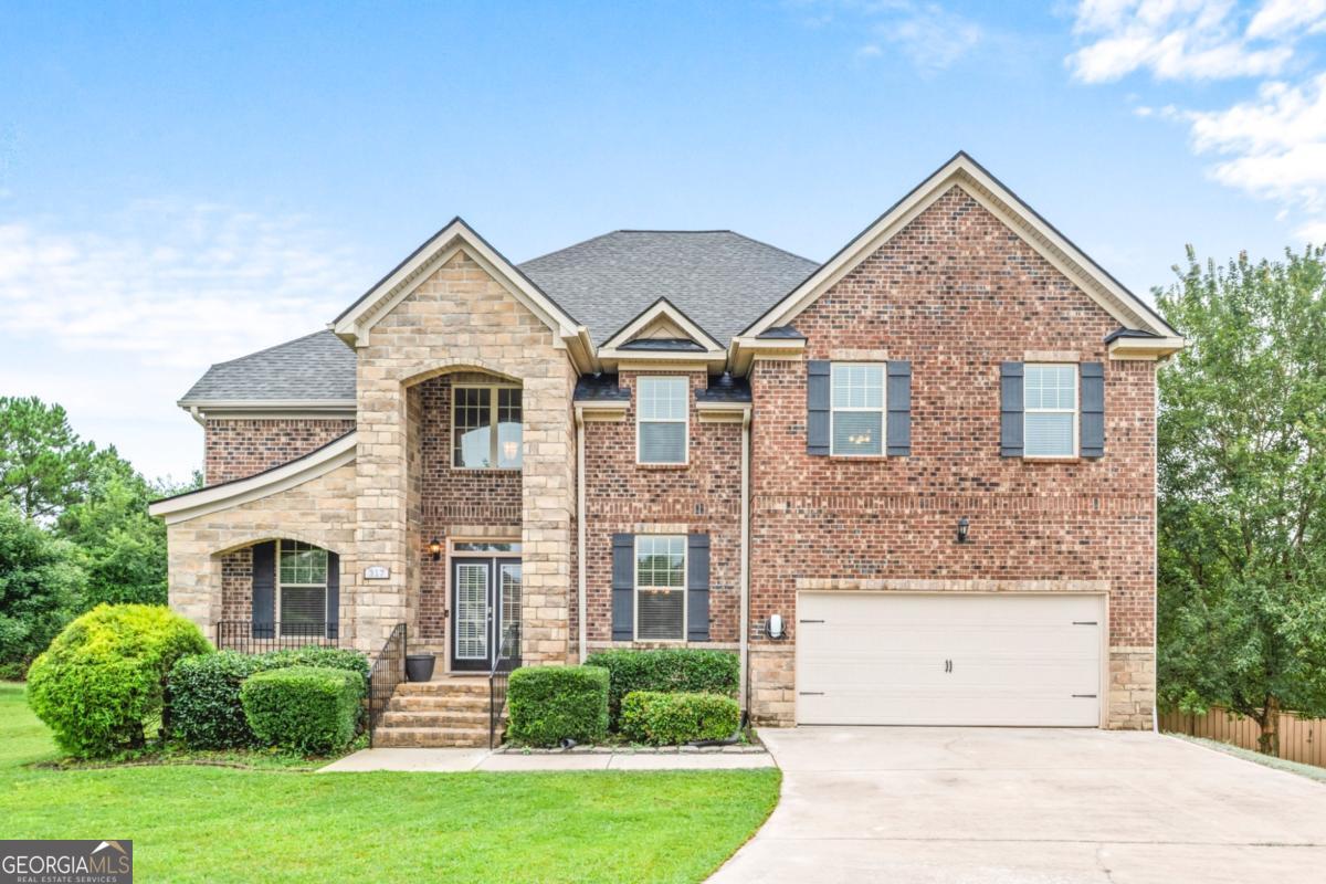 Welcome to 317 Hitt Trace-a stunning full-brick home offering 6,341 square feet of beautifully designed living space, perfectly positioned at the entrance of a peaceful cul-de-sac in the sought-after East Lake Estates community. Within walking distance to the top-rated Union Grove School District, this 5-bedroom, 4-bathroom residence blends spacious living, thoughtful upgrades, and timeless style. Inside, a well-designed layout offers a main-level bedroom with an adjoining full bath-ideal for guests or multi-generational living. The chef's kitchen is a true centerpiece, boasting double ovens, ample counter space, a built-in desk for paying bills or organizing the home, and an open view into the cozy family room. Here, a dramatic stacked-stone fireplace is framed by an elegant coffered ceiling, while rear stairs provide private access to the owner's suite. Just off the garage, a practical mudroom with a built-in bench keeps life organized and clutter-free. Entertain in style in the formal dining room, complemented by a convenient butler's pantry. Upstairs, the oversized owner's suite serves as a private retreat with a generous sitting area anchored by a second fireplace, and the entire second level is refreshed with brand-new carpet for a clean, move-in-ready feel. The fully finished daylight basement-completed in 2020 with Henry County permits-was designed for both functionality and fun. Highlights include ceiling speakers for an immersive entertainment experience, a stacked-stone bar, a closet for a stackable washer and dryer, a private gym enclosed with sleek solid-glass doors, a bedroom with an adjoining full bath, a dedicated home office, and a living area off the bar that's already pre-wired for a home theater. Outdoors, enjoy a fully fenced backyard perfect for pets, play, and quiet evenings. A spacious 2-car garage, manicured landscaping, and exceptional curb appeal complete this remarkable property. Don't miss your opportunity to own in one of Henry County's most desirable communities!