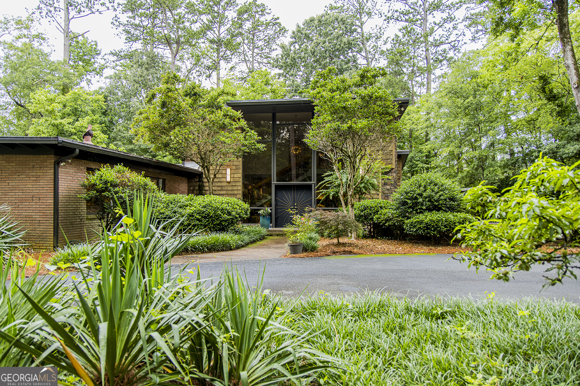 Step into timeless elegance with this stunning 1956 mid-century modern home, thoughtfully renovated to preserve its architectural heritage while offering today's luxury. Tucked away on 1.36 private, park-like acres along scenic Horseleg Creek in the historic College Heights neighborhood, this five-bedroom, four-bathroom residence is a true showstopper. From the moment you arrive, you'll be captivated by the striking two-story windows and custom sunburst-design entrance doors-an homage to the home's original 1950s styling. Inside, a dramatic open staircase with polished wood railings anchors the foyer, showcasing the sophistication of true mid-century architecture. A glamorous sitting room with a wood burning fireplace sets the tone when you enter, while the light-filled kitchen features a sunny breakfast area and flows seamlessly into the wood-adorned dining and living rooms. The living room is expansive and welcoming, with a beamed ceiling, gas log fireplace, and walls of windows that invite the lush natural surroundings inside. The main-level owner's suite is a serene retreat, complete with a spa-like bathroom offering a soaking tub, walk-in shower, and dual vanities. A versatile bonus space with a wooden ceiling-perfect for a home office, sunroom, or yoga studio-extends from the suite and opens onto a private deck. Two additional bedrooms and a full bath are also located on the main floor. Upstairs, two spacious suites each enjoy their own beautifully appointed private bathrooms, offering comfort and privacy for family or guests. Outside, entertain with ease around the fire pit, dine al fresco in the courtyard, or simply enjoy a quiet morning surrounded by nature. A detached two-car garage adds convenience and extra storage. With its impeccable renovation, classic lines, and rare setting, this home is more than a place to live-it's a legacy.