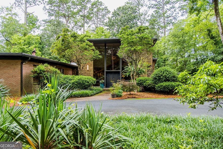 Step into timeless elegance with this stunning 1956 mid-century modern home, thoughtfully renovated to preserve its architectural heritage while offering today's luxury. Tucked away on 1.36 private, park-like acres along scenic Horseleg Creek in the historic College Heights neighborhood, this five-bedroom, four-bathroom residence is a true showstopper.    From the moment you arrive, you'll be captivated by the striking two-story windows and custom sunburst-design entrance doors-an homage to the home's original 1950s styling. Inside, a dramatic open staircase with polished wood railings anchors the foyer, showcasing the sophistication of true mid-century architecture.    A glamorous sitting room with a wood burning fireplace sets the tone when you enter, while the light-filled kitchen features a sunny breakfast area and flows seamlessly into the wood-adorned dining and living rooms. The living room is expansive and welcoming, with a beamed ceiling, gas log fireplace, and walls of windows that invite the lush natural surroundings inside.    The main-level owner's suite is a serene retreat, complete with a spa-like bathroom offering a soaking tub, walk-in shower, and dual vanities. A versatile bonus space with a wooden ceiling-perfect for a home office, sunroom, or yoga studio-extends from the suite and opens onto a private deck. Two additional bedrooms and a full bath are also located on the main floor.    Upstairs, two spacious suites each enjoy their own beautifully appointed private bathrooms, offering comfort and privacy for family or guests.    Outside, entertain with ease around the fire pit, dine al fresco in the courtyard, or simply enjoy a quiet morning surrounded by nature. A detached two-car garage adds convenience and extra storage.    With its impeccable renovation, classic lines, and rare setting, this home is more than a place to live-it's a legacy.