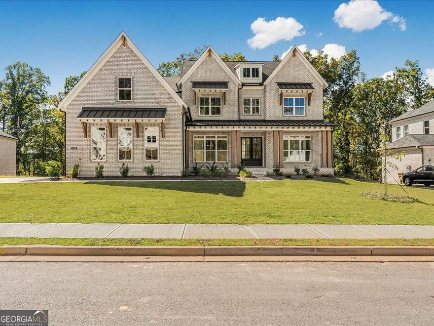 Set within Brookmeade, a coveted Toll Brothers community, this striking brick home combines timeless elegance with quiet privacy on a serene, nearly cul-de-sac street. A wide, covered front porch with double doors opens to a soaring foyer showcasing the elegant upstairs catwalk and a wall of six picture windows that frame wooded views and fill the home with natural light. Flanking the entry are a private office/study and a refined dining room that connects to the fireside family room through a well-appointed butler's pantry and bar. The family room's stacked-stone fireplace rises dramatically to the ceiling, while a three-panel slider opens to a covered porch and adjoining grilling deck both overlooking a flat, private backyard.  The chef's kitchen is a showpiece, featuring waterfall quartz countertops, illuminated ceiling-height cabinetry with glass fronts, a pot filler, Wolf appliances, a spacious walk-in pantry, and a convenient side entry leading to the mudroom and three-car garage with two EV charging outlets. An adjacent secondary prep kitchen/scullery adds a second gas cooktop, room for an additional refrigerator, and abundant storage - ideal for effortless entertaining. A main-level guest suite with en-suite bath offers flexibility, complemented by a stylish powder room for visitors. Additional upgrades include whole-home audio, irrigation system, and a tankless water heater for energy efficiency.  Upstairs, gleaming hardwoods run throughout. The airy catwalk overlooks the main living area and leads to an indulgent primary suite with a cozy sitting area and stone fireplace, two generous walk-in closets, and a spa-inspired bath featuring an oversized rain shower, soaking tub, and extended double-sink vanity. Four additional bedrooms - each with a beautifully finished private bath ensure space and comfort for all. The daylight terrace level, currently unfinished, offers abundant natural light with multiple windows walks out to a covered patio.  The space is an inspiring canvas for a future lounge, gym, media room, or guest suite. Additional perks include a central vacuum system and superior brick construction for lasting quality and peace of mind. Residents of Brookmeade enjoy premier swim and tennis amenities and a prime Forsyth County location within the Denmark High School district. Conveniently close to The Collection, Vickery Village, Fowler Park, and the Big Creek Greenway, this nearly new home delivers the perfect balance of sophistication, privacy, and modern luxury.