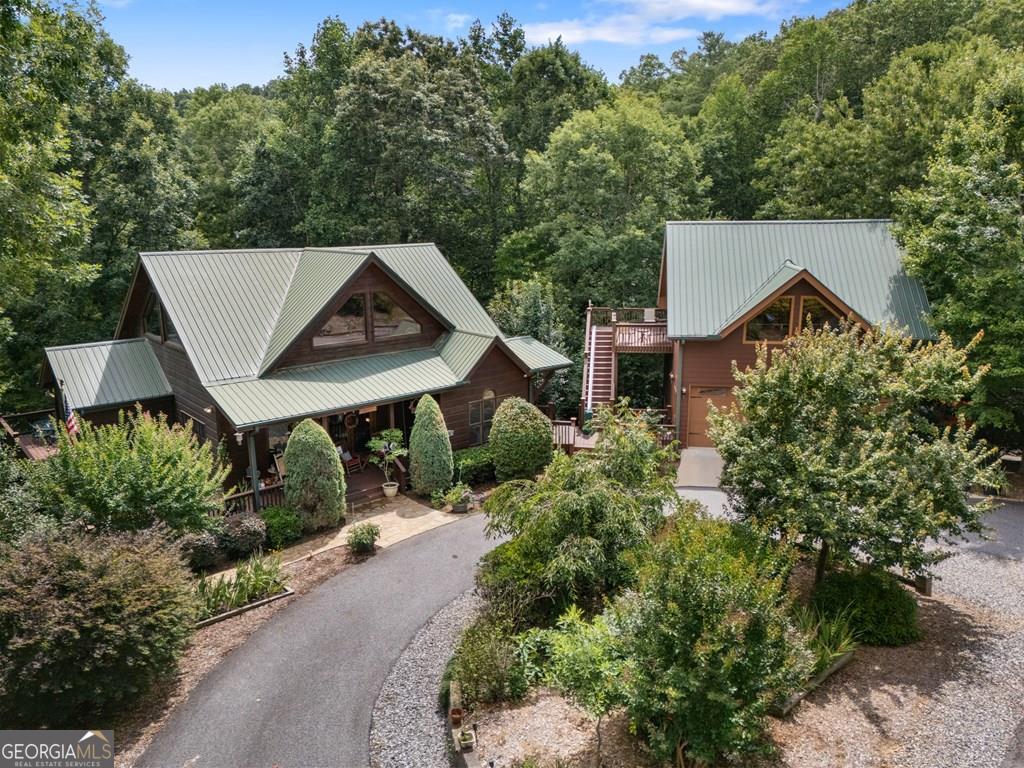 Stunning Spacious North GA Mountain Retreat with Unique Architecture & Modern Amenities! Nestled in a serene setting, this expansive approx. 3,684 sq ft home offers a perfect blend of luxury, comfort & unique design. Arrive via a circular driveway to a spacious covered deck that sets the tone for this remarkable property. Main Level: Step inside to soaring 2 story ceilings, exposed beams & distinctive architecture that define the open-concept living space. The great room, complete w/ a cozy fireplace, flows seamlessly into the dining room & modern kitchen, creating an inviting atmosphere for entertaining or relaxation. The master suite on this level features a generous walk-in closet & a luxurious en-suite bathroom w/ a jacuzzi tub & shower. Step outside to an elevated covered deck, connected to a large, open entertainment side deck, offering breathtaking views of vibrant seasonal plantings & trees. Loft Level : Ascend to the loft level, where a spacious bedroom w/ a walk-in closet & private bathroom awaits. The open sitting area overlooks the great room below, creating a cozy yet airy retreat. Lower Level: The lower level is designed for versatility & comfort, featuring a bedroom w/ a walk-in closet, a full bathroom, a den, & a spacious recreation area w/ a convenient wet bar. This level opens to a lower patio, complete w/ a hot tub & firepit, overlooking a beautifully terraced backyard w/ seasonal views. Three-Story Garage & Additional Living Space: Connected to the main house by decks and walkways, the 3 story garage is a standout feature. The main level offers a 2 car garage w/ ample storage. Above, a stunning 548 sq ft open room w/ cathedral ceilings, hardwood floors, a bathroom & a large closet serves as an ideal guest suite or studio. The lower level offers an additional car bay & a workshop w/ built-in cabinets & stained pine tongue-and-groove walls. Adjacent to the garage, a concrete basketball half-court adds a fun, active touch & abundant parking.