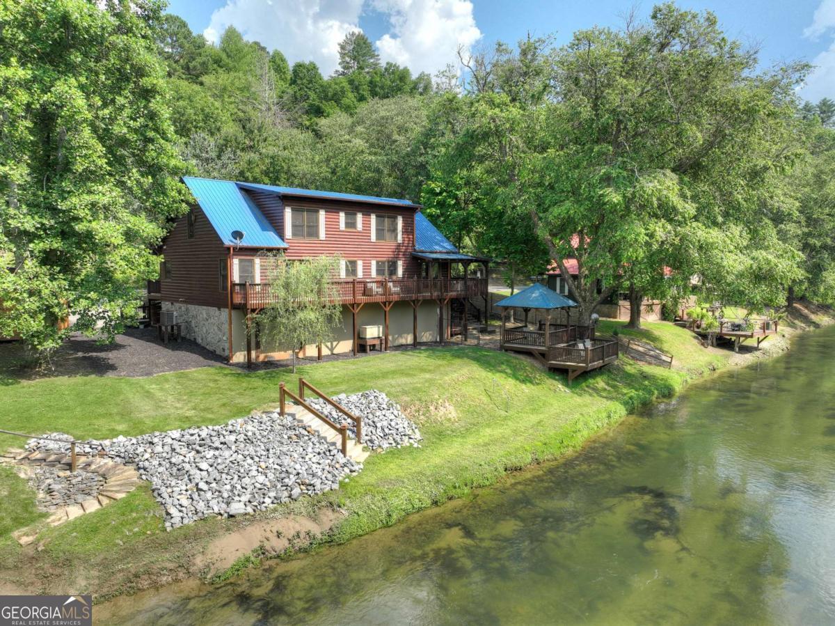 Nestled directly on the banks of the pristine Toccoa River, 946 Fish Trap Trail is a rare riverfront jewel offering an immersive and serene mountain lifestyle. This authentic log-sided retreat captures the magic of daily river life-where fly fishermen cast for trophy trout, kayakers glide along crystal waters, and geese skim the surface at dusk. Boasting 100 feet of direct river frontage, the level, landscaped grounds create the perfect setting for outdoor living with multiple vantage points to soak in the scenery: a riverside gazebo and deck, a firepit lounge, covered porch, and jacuzzi lower patio-all set to the soundtrack of the flowing Toccoa. Inside, the warm and welcoming cabin features an open-concept great room anchored by a soaring stone fireplace and cathedral ceilings, all framed by generous windows with breathtaking river views. The spacious kitchen and bay-windowed dining area overlook a dramatic riverbend-ideal for entertaining with ease and comfort. The home offers 2 bedrooms and 2 baths on the main level, plus a full suite upstairs with an additional bedroom, bath, and expansive loft space perfect for guests, office, or recreation. Whether you're seeking a private riverside escape, a vacation rental with exceptional appeal, or a peaceful primary residence-this riverfront haven delivers rustic elegance and an unbeatable location in the heart of the North Georgia Mountains.