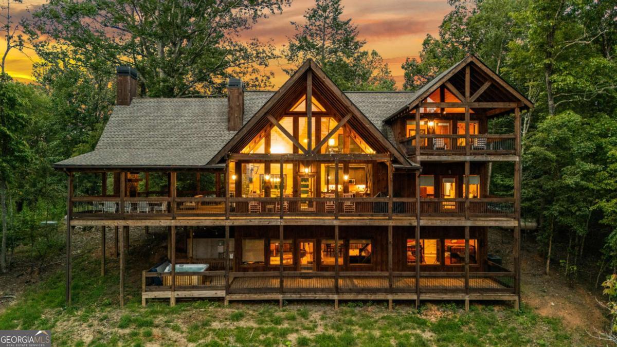 Commanding one of the most spectacular views in the tri-state area, this luxury 3-bedroom, 3.5-bath lodge-style cabin offers an unforgettable mountain experience with layered, panoramic vistas as far as the eye can see. Expertly crafted with a blend of rustic sophistication and artisan detail, the home features soaring ceilings, a dramatic wall of windows, rich rough-sawn finishes, and high-end touches throughout-including custom cabinetry, granite countertops, and designer lighting and fixtures. The owner's suite is privately located on the upper level, offering direct access to a cozy sleeping porch and elevated views of the surrounding landscape. Designed for both comfort and entertaining, the expansive layout includes multiple porches and decks, an oversized party porch with a massive wood burning stone fireplace, and a cozy sleeping porch off the owner's suite. The main level also features a wood burning fireplace inside, creating a warm and inviting gathering space. The fully furnished terrace level provides a private guest retreat, a spacious rec room, and a gas log fireplace, making it ideal for hosting family, friends, or vacation guests. Surrounded by mature hardwoods and lush, gentle landscape, this private mountain-top retreat also features a jacuzzi on the deck-the perfect place to take in the stunning surroundings. Whether you're seeking a luxury getaway, an income-generating short-term rental, or a showpiece mountain home, this one delivers the ultimate in elevated mountain living.