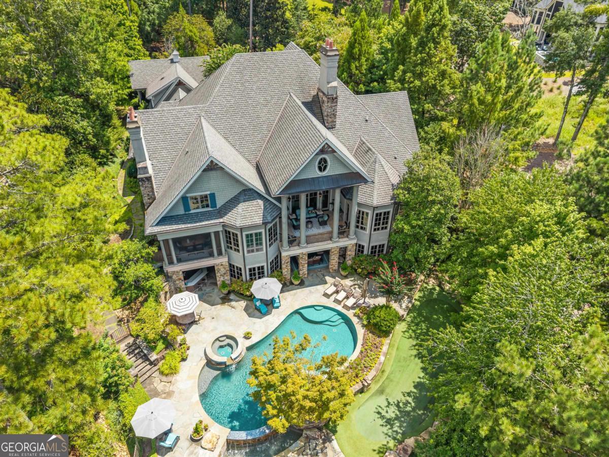 EXPERIENCE ELEGANCE AND COMFORT IN THIS NEWLY REFRESHED MULTIGENERATIONAL LUXURY LAKEFRONT ESTATE IN REYNOLDS LAKE OCONEE OFFERING YOUR OWN RESORT AMENITIES. From the moment you drive down your winding driveway, you are greeted with immacuate landscaping and total privacy. A two story foyer introduces the home and opens to the great room, where a stone fireplace and expansive windows frame the lake. The library just off the foyer is stunning and showcases floor to ceiling bookshelves with a hidden door leading to the primary suite hallway. The suite features a striking domed tray ceiling with exposed beams, expansive bayed windows framing lake views, porch access, a luxurious bath with tiled shower ceiling, soaking tub, dual vanities, his and hers walk in closets, and a private laundry room. Spanning three levels connected by elevators, the home was designed for both gathering and retreat. The kitchen is equipped with Wolf appliances, SubZero refrigeration, a quartz island, and a walk in pantry that doubles as a second office with SubZero freezer. A scullery with additional sink, refrigeration, and dishwasher provides seamless prep for hosting. The dining room and keeping room with fireplace create a relaxed sitting room, while newly refinished hardwood floors and new lighting give the interiors a fresh, modern feel. Upstairs, a full in law suite offers its own kitchen, living area, bedroom, and bath with a private laundry. Two additional guest suites, each with ensuite baths, complete this level and comfortably host family or friends. The terrace level is dedicated to recreation and wellness with a billiard room, poker and game room, custom bar, wine cellar with tasting room, sauna, steam shower, and fitness studio. Outdoor living includes an infinity edge pool, full kitchen and bar, stone fireplace, firepit, private putting green, granite seawall, and a private boat dock on Lake Oconee. Extra features include four laundry rooms including one in the guest apartment, a three car garage with hydraulic lift, geothermal systems, generator, central vacuum, and smart home technology. This is a rare opportunity to own a newly refreshed custom lakefront retreat that blends multigenerational living with the lifestyle of a private resort at Reynolds Lake Oconee. Minutes to the Ritz Carlton, Lakeclub, and all amenities by boat or by car. Membership available.