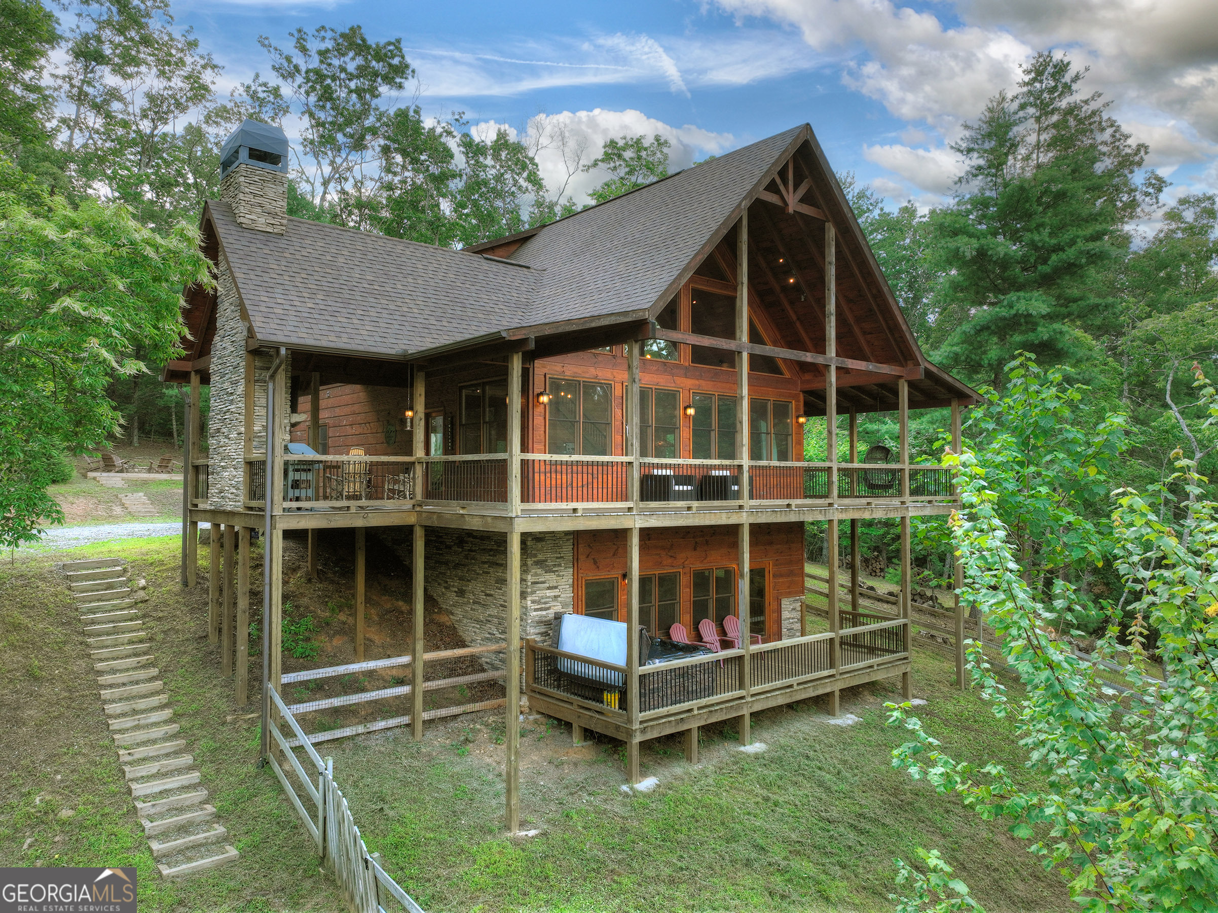 Sleek, stylish, and seamlessly blended with nature-this modern mountain cabin delivers the perfect balance of comfort, luxury, and stylish design in the heart of the highly sought-after Aska Adventure Area. Privately tucked on 2.14 acres in a gated upscale community, this thoughtfully designed retreat features 3 spacious bedrooms, a versatile sleeping loft (ideal as a 4th bedroom), 3 full baths, and a thoughtfully designed half bath with laundry. Step inside to an open-concept living space with vaulted ceilings, floor-to-ceiling windows, and a soaring floor to ceiling stone fireplace that anchors the great room while showcasing long-range mountain views. The gourmet kitchen features clean lines, upgraded stainless appliances, and ample space for entertaining. Both the main and upper levels offer primary suites with large, ensuite baths-plus direct access to outdoor living spaces. The upper suite includes a private balcony, while the main level extends to a wrap-around deck and screened party porch with a cozy wood-burning fireplace-a perfect modern take on classic mountain living. The finished terrace level offers 9 foot ceilings, a stylish wet bar, guest quarters, and a relaxed lounge with fireplace, opening out to the hot tub deck and professionally designed firepit area. With multi-level decks, clean architectural lines, and a sophisticated natural palette, this home is equal parts mountain hideaway and modern getaway, all just minutes from downtown Blue Ridge, award-winning wineries, Toccoa River adventures, and endless hiking trails. Perfect as a full time residence, second home, or investment opportunity, this is more than a cabin-it's your modern mountain lifestyle realized.