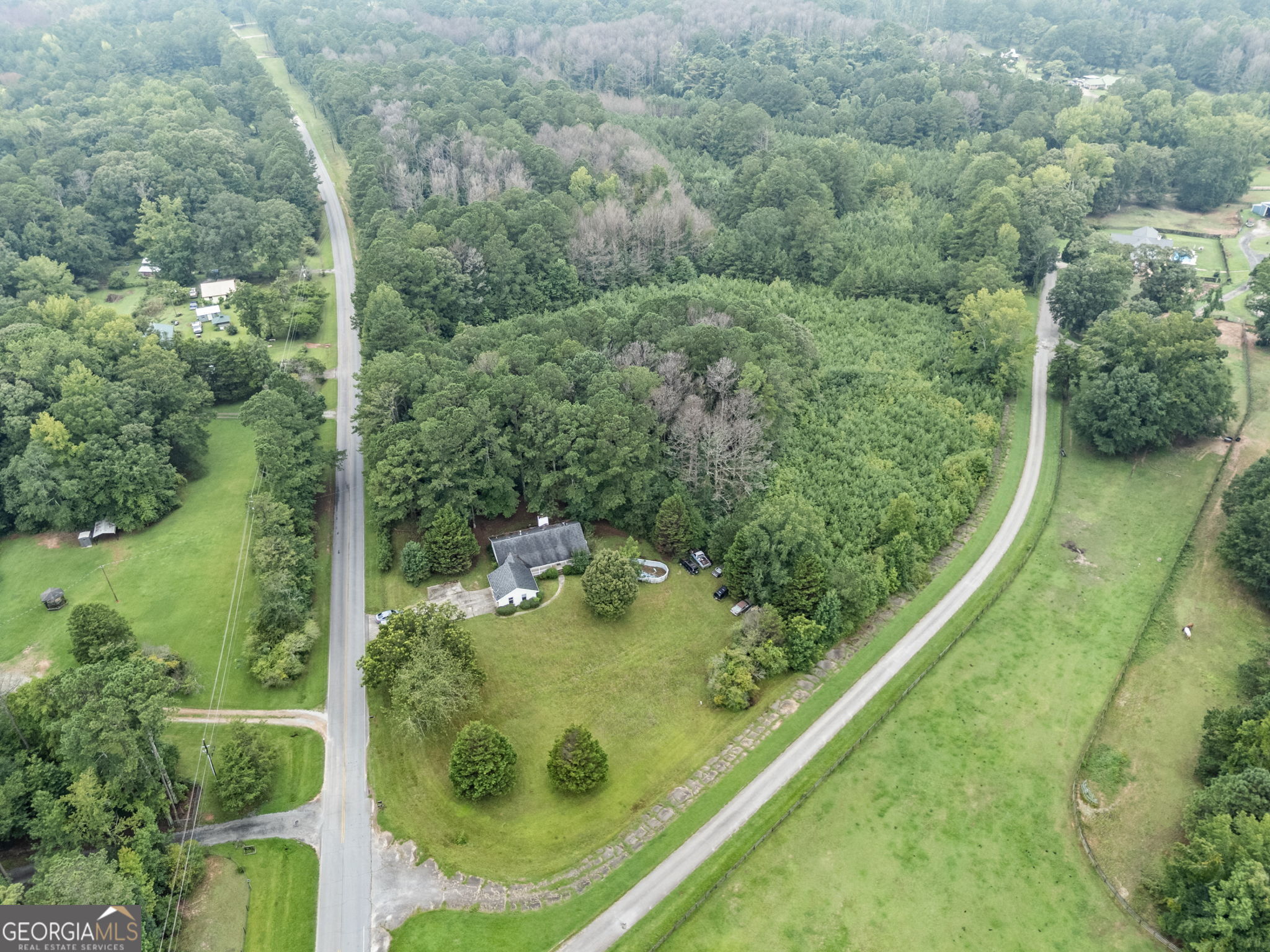 10.2 acres in Coweta's Rural Conservation District. The existing ranch home with basement is a fixer-upper, ready for full remediation + renovation or total redevelopment. The main level of the home features hardwood floors and stone masonry details, 3 bedrooms, 2 full bathrooms, a separate dining room, a living room with a wood-burning stove fireplace and sliding door to the back deck, and a country kitchen with direct access to the two-car garage. The basement, already partially finished, could be completed as a full suite with 2 bedrooms, a bathroom, living room, kitchenette, and storage. Outside, the property offers a large parking pad, a lush lawn, and beautiful views of the neighboring equestrian property. Situated on a quiet corner lot, it provides the peace of rural living while being only 15 minutes from downtown Newnan. With over 10 acres, there's potential to subdivide into two 5-acre estate lots (buyer to verify) or keep as one expansive tract. RC zoning also supports agricultural and equestrian uses, providing multiple ways to add value. Any cars on-site will be removed before closing.