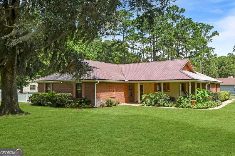 Welcome to this beautifully maintained 3-bedroom, 2-bath brick home offering 2,200 sq. ft. of comfortable living space on a large .52-acre corner lot. Surrounded by gorgeous landscaping, this property features a partial wraparound front porch and a fenced backyard with an irrigation system, providing both curb appeal and outdoor enjoyment. Step inside to find Hickory hardwood floors flowing through the spacious layout with carpet in the bedrooms. The large kitchen boasts abundant cabinetry and a sunny breakfast room, perfect for casual meals, while the formal dining room is perfect for special gatherings or you can use it as a home office, library or additional living space. The inviting living room with fireplace creates a warm and welcoming atmosphere, complemented by a bright, enclosed sunroom for year-round relaxation. Additional highlights include spacious bedrooms, a new metal roof, and a big garage with an oversized driveway, providing plenty of parking. Located in a no-flood zone, this home offers peace of mind along with timeless charm.