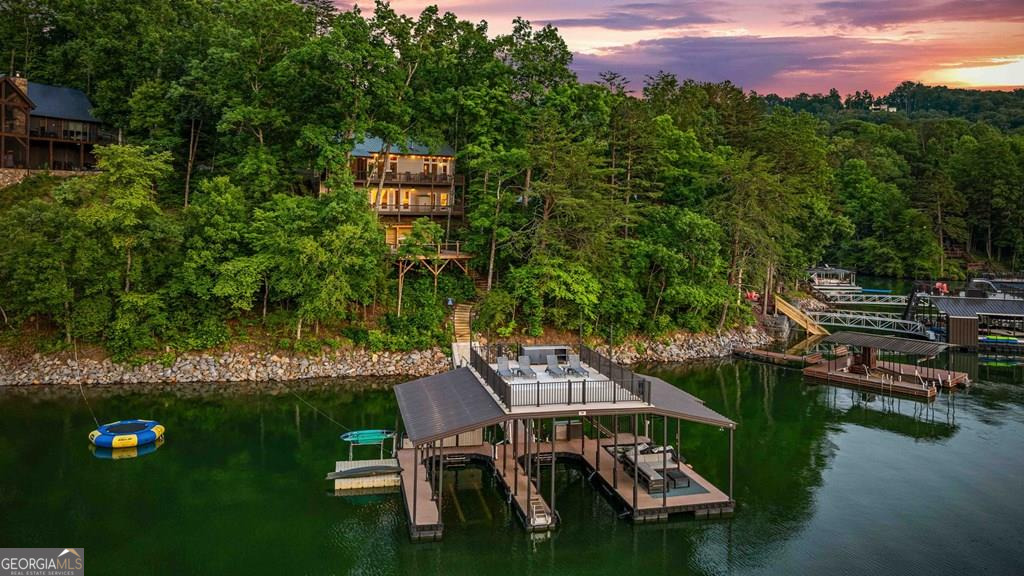 Lake Blue Ridge retreat featuring year-round deep water and breathtaking long-range lake and mountain views. This 4-bedroom, 3-bath getaway offers an open-concept kitchen and dining area with butcher block countertops, stainless steel appliances, and pantry. The great room showcases a gas log fireplace and a wall of windows framing the lake. The main-level primary suite features floor-to-ceiling windows and vaulted wood ceilings, creating a warm and inviting escape. A guest bedroom with a custom kids' loft offering additional sleeping space, along with a full bath, completes the main level. The terrace level includes a game room, bunk room, additional bedroom, full bath, and laundry-ideal for hosting family and friends. Outdoor living shines with a screened porch and an impressive waterside deck featuring a fire pit, bar, ice maker, and beverage cooler-perfect for entertaining or relaxing by the water. The crown jewel of this property is the Wahoo double-decker, two-slip dock with a boat lift, PWC ports, kayak rack, sun deck, and generous seating-ready to enjoy all year long. Easy, mostly paved access and just minutes from historic downtown Blue Ridge. Whether you're seeking a private lakefront escape or a turnkey short-term rental investment, this is a rare opportunity on one of Georgia's most coveted lakes.