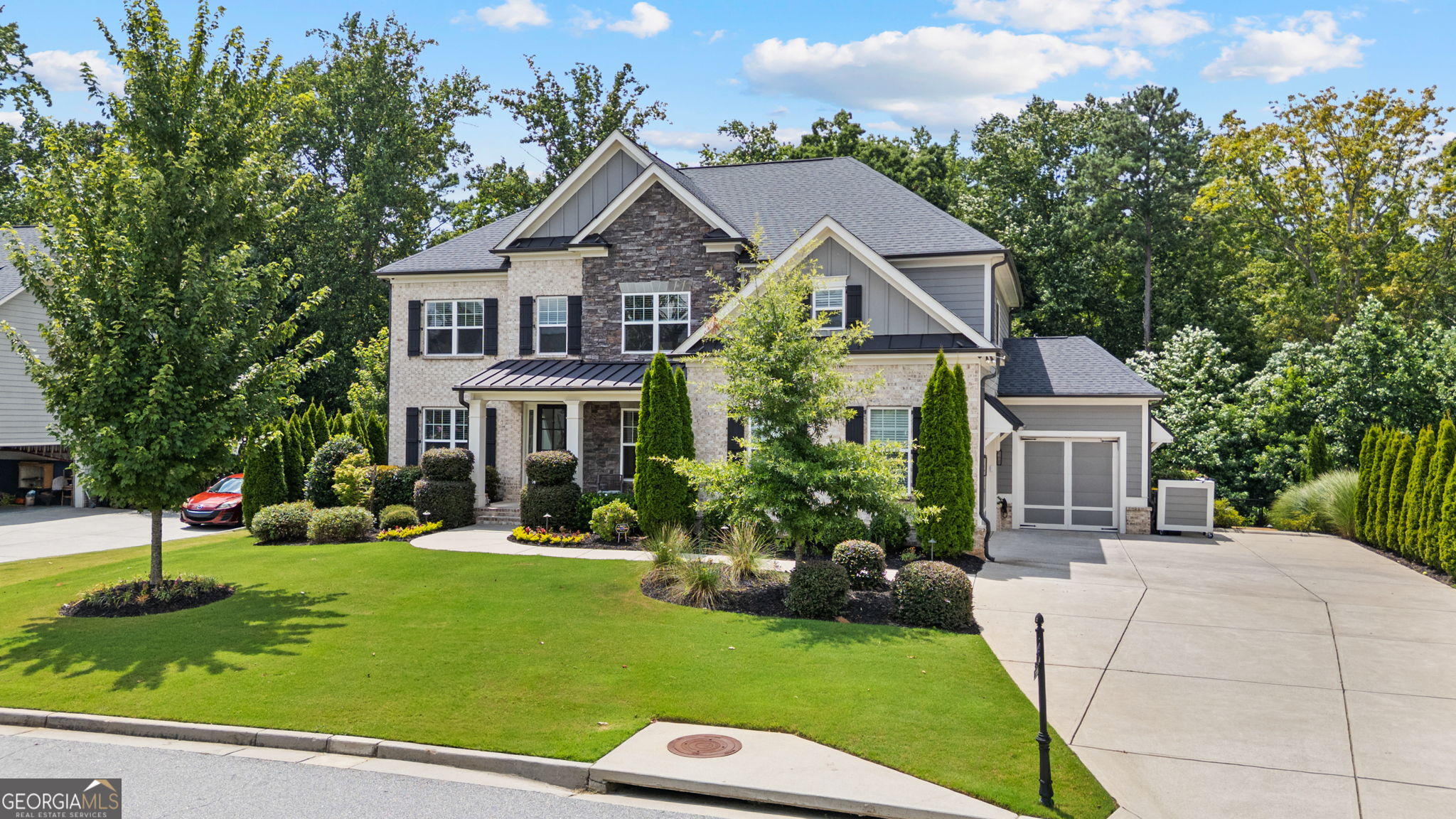 Tucked away in a sought-after community, and priced below appraised value, this expansive 6-bedroom, 4.5-bath, 3 car garage estate on a FULLY FINISHED TERRACE with a SECOND KITCHEN AND LAUNDRY redefines luxurious living with over 5,500 square feet of space. The stacked stone, brick, and board-and-batten exterior creates a stunning contrast that highlights the inviting covered front porch. Auto enthusiasts will appreciate the garage's unique features, including 8-ft doors, pure white polyaspartic epoxy floors, slat wall organization, and a third carriage garage pre-wired for a 4-post lift. Add in a mounted commercial-grade opener and an integrated EV charger, and you've got the ultimate setup for storage, tinkering, or showcasing your prized vehicles. Inside, discover wide-plank engineered hardwood flooring that spans the entire home. French doors open into a formal living room or possible home office. The open layout is anchored by a true chef's kitchen, outfitted with top-of-the-line Wolf appliances, a large island, sleek cabinetry, and generous counter space. Whether you're hosting a dinner party or cooking a quiet meal, this kitchen is built to perform, with a connected vaulted sitting room and effortless flow onto the deck. Natural light floods the adjoining family room, highlighting the clean lines of the coffered ceiling and the cozy fireplace. A dry bar, half bath, and a full main level en-suite complete the first floor. Upstairs, you'll find a dedicated media room, the perfect retreat for movie nights, gaming, or even a workspace. The oversized primary suite is complete with French doors leading into the vaulted bath with a walk-in tiled shower, soaking tub, and double vanity. Spacious secondary bedrooms feature walk-in closets and stylish finishes that cater to both comfort and style. Refinished hardwoods continue through the hallway, maintaining consistency and quality throughout. The finished terrace level offers a completely self-contained living space, ideal for in-laws, extended guests, or long-term multi-generational needs. Enjoy a full kitchen with a rolling island, farmhouse sink, gas cooktop, and excellent storage. There's also a private bedroom suite, separate laundry area, and a flex space. A massive bonus room provides endless options when utilizing this space to meet your lifestyle. Custom built-ins and large windows make this lower level feel just as polished and bright as the main floors, with access to a beautiful brick paver patio. Enjoy evenings on the upgraded back deck, which comes ready for your gas grill. The wrought-iron fenced backyard provides a modern look with peace of mind. A custom flagstone pathway and steps lead from the backyard to the driveway for added convenience while hosting, making it as functional as it is attractive. Professionally landscaped around the entire property, complete with in-ground irrigation and accent lighting. Four perimeter security cameras with DVR backup provide 24/7 monitoring, while LED lighting throughout boosts energy efficiency without sacrificing style or charm. From its high-end finishes to its versatile layout, this residence delivers the ultimate package without compromise-whether you're accommodating guests, working from home, or relaxing in style.