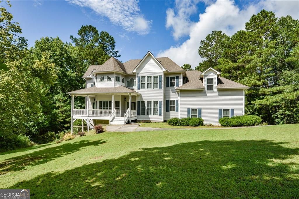 Southern charm meets modern living! This 4-bedroom, 3 full/2 half bath home on 4.3+ private acres offers wraparound covered porches, timeless curb appeal, and a thoughtful floor plan designed for comfort and style. Inside, hardwood floors flow from the foyer to a formal dining room and a flex room with custom moldings. The living room features a cozy fireplace with a wood shiplap accent wall, opening to a gourmet kitchen with granite countertops, stainless steel appliances, tile floors, tile backsplash, walk-in pantry, raised bar seating, and a gas range. A bay-window breakfast nook overlooks the backyard, and French doors lead to an expansive back deck. The mudroom off the 3-car garage includes a custom bench, built-in storage, and utility sink. Upstairs, the primary suite boasts a fireplace, private balcony, huge walk-in closet, and a spa-style bath with French doors, double vanities, a garden tub, and a double-headed custom tile shower. Two bedrooms share a Jack-and-Jill bath, and the fourth bedroom is an expansive, versatile space-perfect for a media room, playroom, home gym, or retreat. The full, partially finished basement is stubbed for a bath with a sink and commode already in place, plus a boat door, utility sink, and space ideal for a workshop or boat/golf cart parking. From here, step out to the covered terrace-level patio and fenced backyard. Privacy, versatility, and Southern style await-prime location with nearby conveniences.