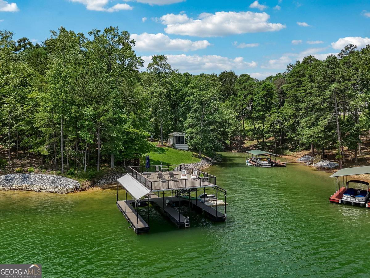 First time on market for this two parcel lake front opportunity! This is a once in a lifetime Lake escape sitting on nearly 2.5 flat and gated acres on the south end of Young deer point, with big water views of Lake Lanier. The property features two docks; a 16x16 Platform and a 32x32 custom double slip, two story party dock, with like new Polly Lift Boat Lift and two ride up Jet Ski lifts, as well as new electric wiring and panel boxes. The purchase includes two separate lots. LOT 1 includes a 3500 sq ft custom designed and built, barn styled farmhouse, Board and Batten siding, new architectural shingle roof, new Andersen windows, a large deck, 1500 sq ft 3 car garage with sprinkler system, epoxy floor and a cleared space outside for an additional barn/workshop. Upon entry you find a large media room with its own full bathroom and garage access, that could double as a guest suite. A grand staircase leads you to the second level that features an abundance of natural light, open floor plan with an L shaped kitchen and stone counters, living room, and a separate dining nook. The second level also boasts the inviting master suite and an additional bedroom and full bathroom. On the third level you discover the two bed loft over looking the cozy family room. Additional interior features all 8 ft doors, full alarm system, hardwood floors, and beautifully detailed crown molding. LOT 2 has been cleared for a custom build opportunity with Power and Water in place for future home or camper/RV hook up. LOT 2 Features also include grandfathered in gravel drive to Lake, mow permit, sprinkler system at grass at shoreline. Also, there is an ADORABLE Picnic House at Waters edge with water, electric, screened in porch and tin roof to enjoy reading a book or listening to the rain as well as a custom fire pit. Property is turn key and ready for you to make whatever your dreams may desire whether it be for personal enjoyment or events and weddings. This property has been loved for over 20 years.. must see to appreciate. This opportunity won't last long . Bring your boats and skis . This is the one.