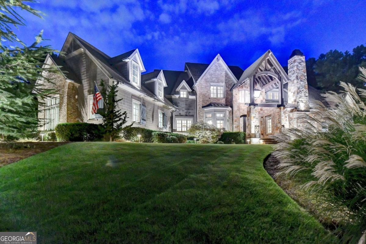 Welcome to this exceptional River Club estate, perfectly positioned between the 5th AND 6TH HOLES of the prestigious Greg Norman GOLF COURSE. This custom-built masterpiece features 5 bedrooms, 6 full and 3 half baths, a MASTER-ON-MAIN, WALK-OUT HEATED SALTWATER POOL, and a finished TERRACE LEVEL -all crafted with meticulous attention to quality and design. Step through the grand stone porch into a foyer flanked by a sophisticated OFFICE with MARBLE FIREPLACE and a DINING ROOM with bay windows and beamed ceilings. The soaring FAMILY ROOM boasts RECLAIMED WOOD BEAMS, a floor-to-ceiling stone fireplace, and views of the POOL and outdoor living spaces. The gourmet kitchen features brick accents, high-end cabinetry, Stainless steel WOLF /SUB-ZERO APPLIANCES, granite island, walk-in pantry, and a wet bar. A sunny BREAKFAST ROOM opens to the COVERED STONE PORCH with FIREPLACE, built-in GRILL, fridge, and full pool bath, ideal for entertaining. The luxurious MAIN FLOOR owner's suite includes a BEAMED tray ceiling, FIREPLACE, bay windows, and spa-like bath with jetted tub, double vanities, walk-through shower, and custom walk-in closet. Additional main-level amenities include a large laundry, mudroom, powder room, and built-in workstation. Upstairs offers a cozy loft, three spacious en-suite bedrooms, a SECOND LAUNDRY, and an unfinished BONUS ROOM. The daylight TERRACE LEVEL is an entertainer's dream with HANDCRAFTED woodwork, brick and wood-paneled walls, SLATE floors, a BAR, GAME room, GYM, GUEST suite, and powder room. Outside, the rare WALK-OUT Pebble-Tec SALTWATER pool features a waterfall, HOT TUB, FIREPLACE, covered patio, and lush landscaping-just steps from the GOLF COURSE. Top-tier features include a DEEP WATER WELL, Generac WHOLE HOME GENERATOR, WATER FILTRATION & HUMIDIFIER systems, app-controlled LUTRON LIGHTING, extensive outdoor lighting, 4 CAR GARAGE & large motor court. Built from the ground up by the ORIGINAL OWNERS with no expense spared, this home is the pinnacle of luxury in Atlanta's premier gated golf/swim/tennis community-The River Club.