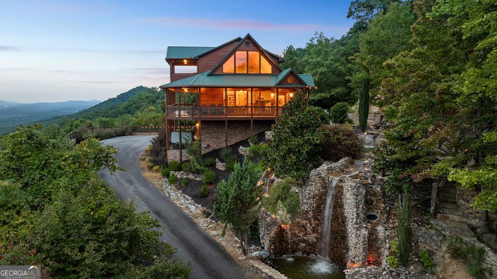 Luxurious mountaintop retreat offering complete PRIVACY and BREATH-TAKING VIEWS! Recently featured on American Dream Home, the Waterfall Lodge boasts panoramic long-range layered mountain views plus the sounds from your very own 25' waterfall for a truly one-of-a-kind mountain experience. Impeccably maintained with absolutely stunning views from every room, this private 4 bedroom mountaintop escape features the primary owner's suite on the main, high-end furnishings and decor, and recently updated finishes throughout. Massive stone fireplace and vaulted ceilings highlight the main living area with terrace level featuring oversized game room with additional family room and bunk room perfect for larger groups. Professionally landscaped and hardscaping with cozy outdoor fire pit area and outdoor spaces designed for entertaining while soaking in the views! Perfect for full-time living, luxury vacation rental, or private weekend getaway, this legacy property is offered turnkey with furnishing included. All paved access, plenty of parking, high-speed internet and backup generator. Waterfall Lodge offers complete serenity in the mountains yet is close enough to enjoy all things Blue Ridge has to offer including shopping, dining, trophy trout fishing, lake Blue Ridge and more!