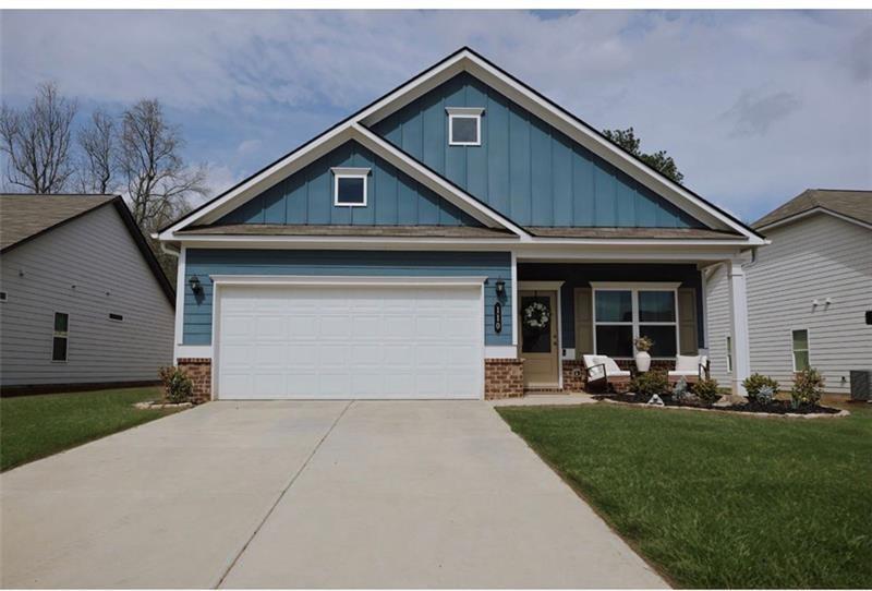 Single-story residence featuring blue siding with board and batten accents, a covered front porch, a two-car garage, brick foundation detailing, and a concrete driveway