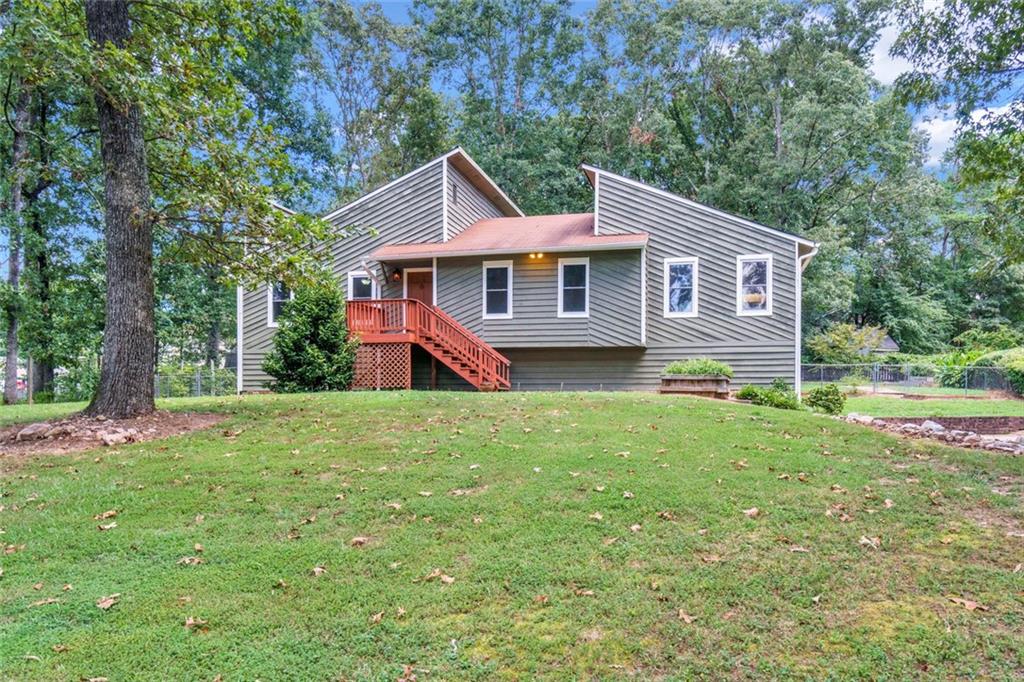 Come discover this lovely, contemporary retreat in an unbeatable location: 1797 Kelvin Drive is a unique raised ranch in the heart of Gwinnett County. This desirable neighborhood is located just minutes from I-85, GA-316, the Mall of Georgia, The Exchange at Gwinnett, Rock Springs Park, and downtown Lawrenceville’s shops, restaurants, and cultural venues.
Inside, you will enjoy the vaulted family room with its charming stone fireplace, parquet hardwoods, and custom built-ins. The kitchen features abundant and freshly painted cabinetry, newer stainless steel appliances, and a window that frames the view of the lush rear yard. Step out to the private deck and experience the peace of your own backyard oasis. The spacious primary suite includes a private bath and a separate dressing area, while two additional bedrooms share a freshly painted hall bath. Downstairs, the partially-finished basement provides ample storage, a large laundry room, and flexible living space with a broadcast-quality recording studio. This incredible feature is a 6x9 pro isolation booth finished with panels of Owens-Corning 703 acoustic fiberglass insulation which was designed by an acoustician. Vocal artists and musicians will appreciate this unique and valuable addition to this wonderful home. The flat, lush yard is truly a hidden gem—fenced and beautifully landscaped with mature trees and expansive greenery that create a sense of serenity. Whether sipping coffee on the deck or gardening in the sun, it provides retreat from the everyday hustle. A large outbuilding adds even more storage for outdoor gear, tools, or weekend projects.