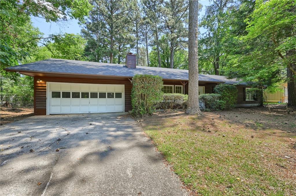 Ranch-style residence featuring brown wood siding, a gray shingle roof, and a two-car garage with a paneled door