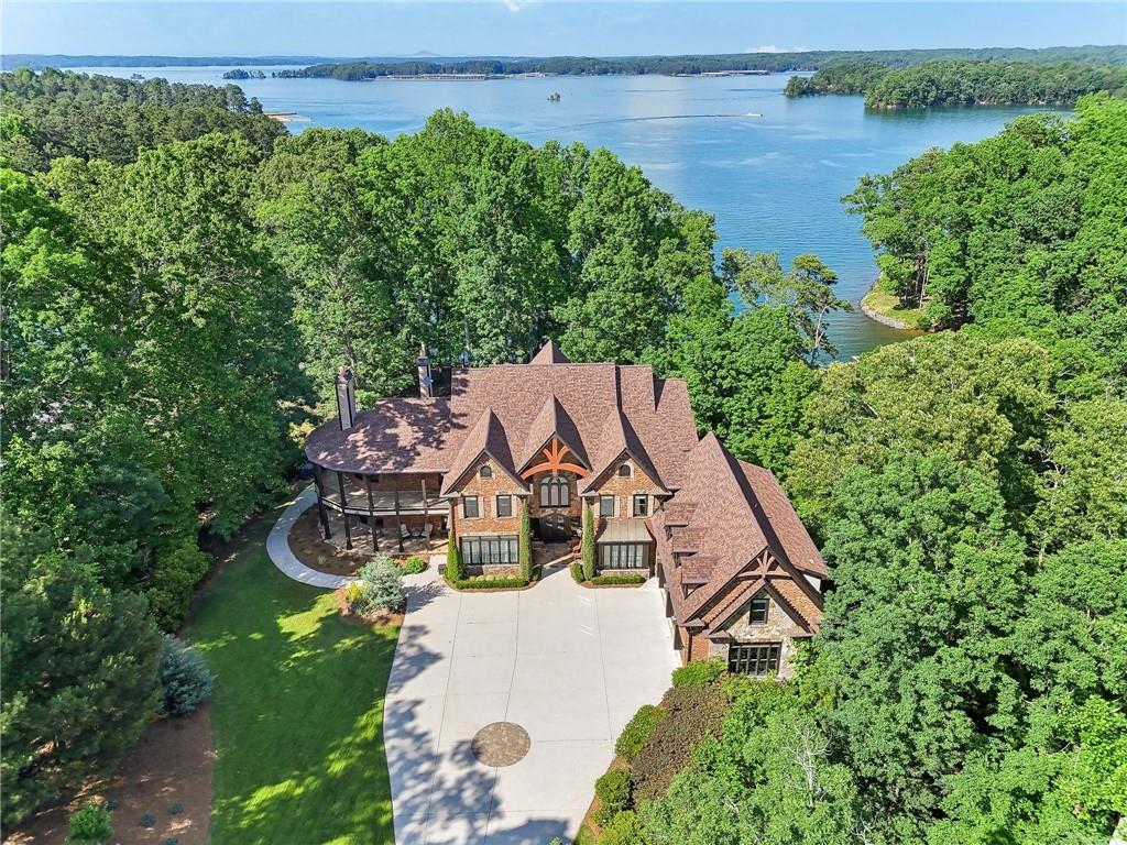 The ultimate in luxury, this luxuriously furnished estate is located on the south end of Lake Lanier, come home to gated privacy on over two wooded acres, relax on two wrap-around verandas or by the newly updated pool. The double slip Martin dock is steps away, with drought-free deep water, to enjoy the jet boat awaiting you for a cruise and water sports! Friends can enjoy the furnished sun deck to watch the activity in the bay. This home was built for entertaining with beautiful views from each of the 6 suites each with private baths and newly installed carpet in each room. The owner’s wing offers luxurious amenities, a completely breathtaking bath with a large shower, tub for two, double vanities, water closet, built in cabinetry, and a door to the upper veranda and a masonry fireplace just for you! The bedroom also offers to ways to access the veranda overlooking the entry and a gorgeous view of the pool and lake! The closet, with customized built-ins to please a king and queen! Relax in the dressing/sitting area with your own utility room outfitted with a folding table and a beverage frig! Cross over the catwalk to the additional suites, an extra half bath, and the apartment-style suite with a full kitchen and two desk cubbies. With over 9800 square feet of four finished levels, each comes fully furnished, so just bring your suitcases! And when you need bedding for the teens coming for the weekend, there is a spacious bunk room up on the fourth floor, with two built-in bunk beds with steps and storage! Again, with a private bath and lake views! Take the elevator back down to the main floor where there are his and her offices, one with a full bath, custom built-ins, and a fireplace in the paneled study. There are a total of six fireplaces, two masonry built outside. Enjoy entertaining in the banquet-sized dining room, butler’s pantry with wine Cuvier, across from the cook’s kitchen with full, top-of-the-line appliances including an ice maker and beverage refrigerator. Adjoining the kitchen is a lovely casual dining space and a great room with a coffered ceiling, a fireplace, and a tucked-in serving bar. Take the masterpiece, circular staircase to the terrace level where friends and family will love the media space, and multiple areas for sitting to chat or watching the movie on the big screen. Nearby are the rooms for billiards, gaming, and exercising. For the wine enthusiast, look under the staircase, where you’ll see through to a temperature-controlled wine room and a cozy tasting corner. There is a security camera system installed throughout the estate. Whole house media system. Three-car extended garage with new SwissTrax flooring installed to please even the most discerning car collector. The exterior has been painted and much of the interior. This home was built on estate sized lots to give total privacy from the road.