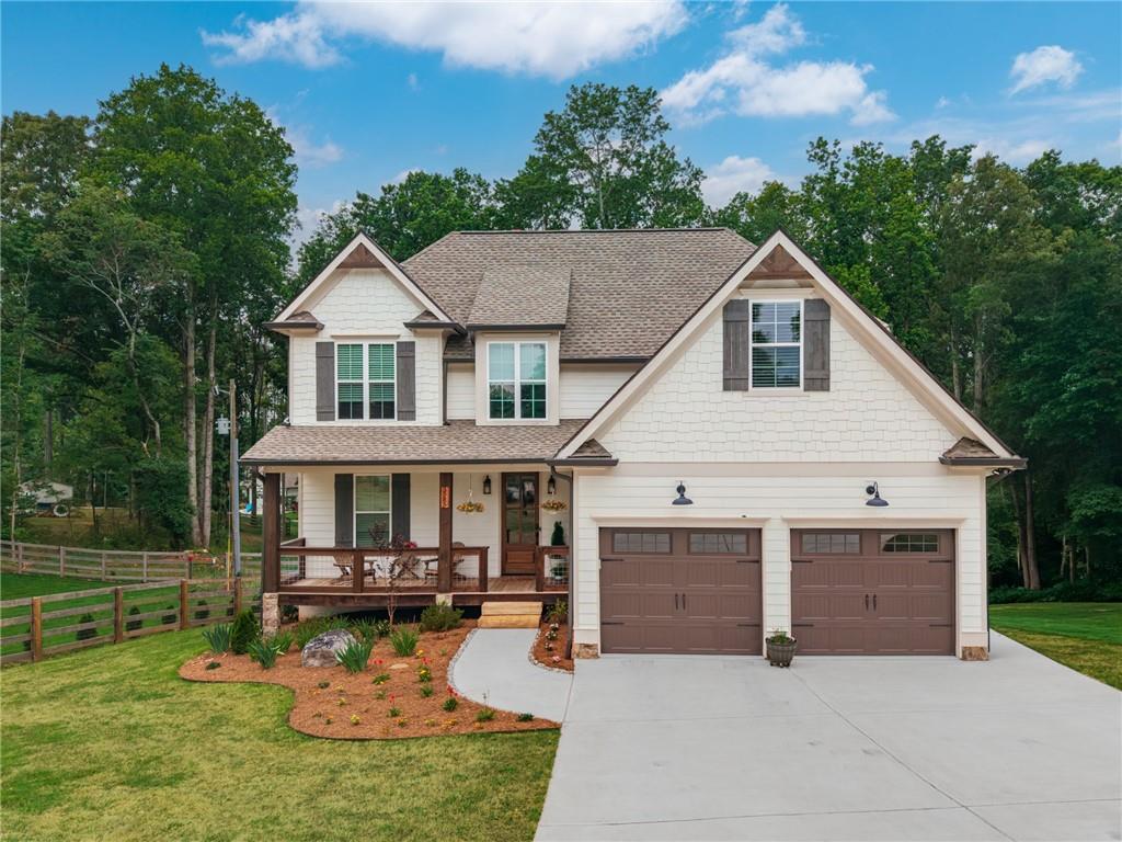 Impeccable curb appeal showcasing stone and board-and-batten accents, a welcoming covered front porch, fresh professional landscaping, and a functional two-car garage with carriage doors.