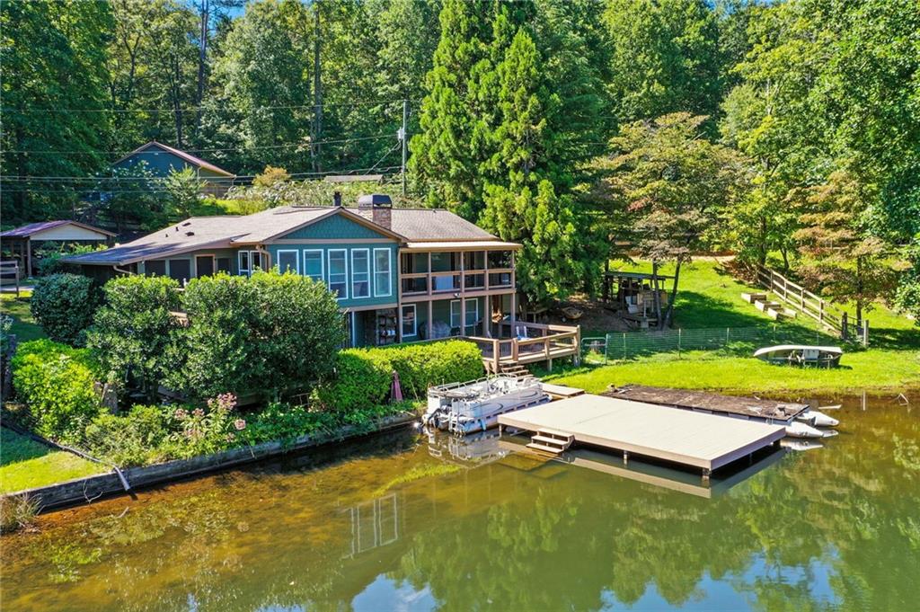 Looking for a hidden gem tucked away in the foothills of the North Georgia Mountains? Here it is! This home is located on a 24-acre lake stocked full of bass, brim, bluegill, crappie, and catfish. Along with the fish, enjoy all that nature has to offer like herons, diving and mallard ducks, resident eagles, king fishers, and other wildlife found in the mountains. When you arrive, you are greeted by a road lined with crape myrtles and shrubbery. The cottage style front porch leads you into an open kitchen and living space with a vaulted white pine tongue and groove ceiling, hand scraped walnut engineered hardwood floors and a wall of windows with a view the entire length of the lake. The sunsets fill the room every evening. The kitchen is equipped with granite counter tops, a double oven with a glass top cooking surface, and a gas range on the island. Right off of the kitchen is a screened porch and BBQ deck, making entertaining a breeze.
Access to a covered deck is right off the front room. The master bedroom is conveniently located on the main floor with its own master bath and walk-in closet. Both upstairs bedrooms have access to the upper deck. The lower level of the home has access to a deck that runs the entire width of the house that leads you to a fenced yard with a large dog house and a 16x24 dock. There are wood burning stoves on both levels of the home and a 15k whole house Generac generator. The lower level could serve as an in-law suite/teen suite with a separate entry/exit off the lower deck. This home has been very well maintained with a new roof and gutters in 2020 & fresh paint on the interior and exterior just recently. The community has a club which is only $300 annually to maintain the lakes and dam! No rental restrictions! This home will not disappoint! ****Additional property available, please inquire!