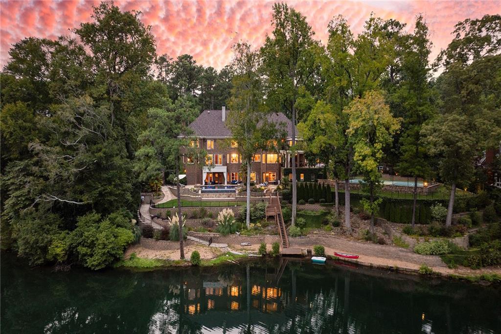 Discover an unparalleled sanctuary with this rare private estate in Sandy Springs, nestled near Chastain Park and Buckhead. Spanning two lush, fully-fenced acres, this exclusive gated property offers breathtaking panoramic lake views that evoke the serene ambiance of Lake Burton, right in the heart of Chastain.
Embrace lakeside living with a private dock, a charming paddle boat launch (electric motor boats permitted), and a lakeside entertainment area featuring a bocce ball court, horseshoe pit, and a cozy fire pit. This home is the epitome of luxury and comfort, featuring an elevator that services all levels, a state-of-the-art movie theater for cinematic experiences, and a wine cellar perfect for showcasing your collection. For wellness enthusiasts, there’s a workout room, a 12-person sauna, and a private 5-person infrared sauna in the primary suite, along with a steam shower for ultimate relaxation.
As you enter the home through the grand, oversized domed foyer, you are immediately welcomed into a main level designed for both elegance and functionality. The open family room seamlessly connects with the kitchen, creating a perfect space for gathering and entertaining. Adjacent to the kitchen, the breakfast room offers a casual dining option with a view. For more formal gatherings, the dining room accommodates at least twelve guests, while an additional covered patio off the kitchen offers another dining alfresco option. This patio can comfortably seat twelve and presents the opportunity to be screened in for year-round enjoyment. The formal sitting room is highlighted by an ornate limestone fireplace, adding a touch of grandeur. The two-story all-wood library or office provides a stunning backdrop for work or relaxation. A versatile bonus room on this level can serve as an additional oversized primary bedroom or a playroom, depending on your needs. Convenience is key with a family entrance located next to the garage entrance, both leading into a well-appointed mudroom. This thoughtful layout ensures that the main level is both practical and inviting, setting the tone for the rest of the home.
The second floor is dedicated to luxurious living quarters, with five spacious bedrooms including the expansive primary suite. The primary suite boasts a private patio with a hot tub and a sitting area with a limestone fireplace. The suite’s his-and-her closets are remarkably large, with a additional separate closet within for seasonal wardrobe changes. The opulent primary bathroom includes dual vanities, a makeup vanity, a full-sized shower, a separate tub, and an infrared sauna. Each of the additional four bedrooms features an ensuite bathroom and walk-in closet, while the upper-level library offers a tranquil space for reading or card games.
The terrace level truly shines as an entertainer’s paradise. It features an in-law suite, wine cellar, theater room, pool table room, workout space, massage room, and a 12-person sauna. This level opens to a stunning stone infinity-edge pool overlooking the lake, with a cabana providing a bonus kitchen and bathroom for guests. A sports court adds to the recreational options.
This home is a true oasis, perfectly designed for both grand entertaining and cherished family moments. From lakeside fireside games to movie nights, basketball, and pickleball, this residence provides an unparalleled living experience.