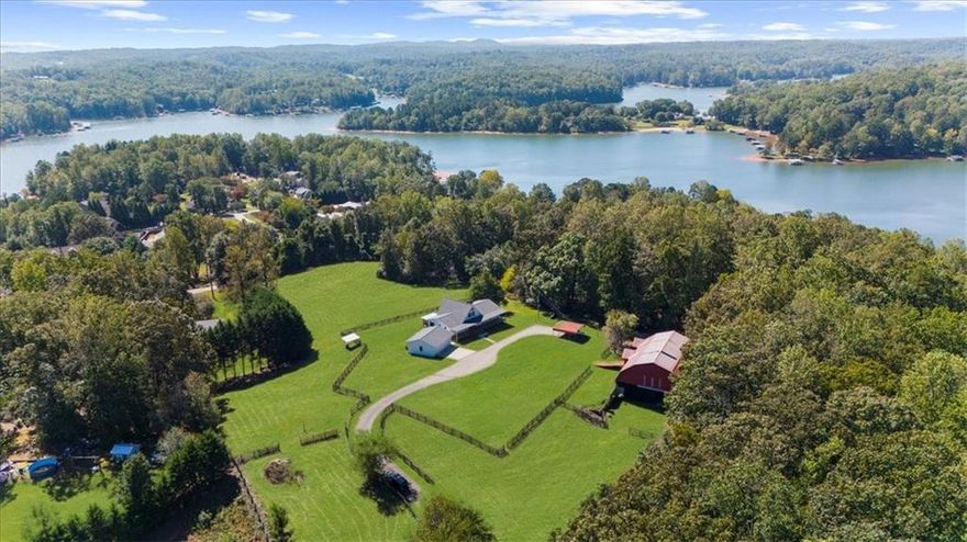 Why settle for land or the lake when you can have both at 518 Overlook Drive? The long, beautiful tree lined driveway leads you to your private gated estate on 7.93 acres with seasonal views of Lake Lanier. This is where you will escape the hustle and bustle life can be and relax at your very own sanctuary of rolling pastures in solitude with your family, friends and farm animals. As you drive in and feel the stress melt away, you are going to love walking up to the charming front porch overlooking the barn and pastures perfect for rocking chairs and a hot cup of coffee in hand. Step inside and be wowed by the soaring vaulted ceilings with natural light pouring through in the great room. Lovely 3" oak floors throughout the main level and loft. The primary bedroom is conveniently located on the main level with picturesque views, brand new, stacking sliding doors (that open all the way) leading to the expansive back deck, and an updated spa-like bathroom. The loft has views overlooking the pastures and lake making it a dreamy office space or an additional sleeping area. The bright and updated kitchen with stainless steel appliances flows into the screened porch where you can cozy up with a nice book and your favorite beverage. The main level also features an updated full bathroom along with a half bath. Make your way downstairs where there is a second kitchen, living room, bathroom and two additional rooms that can be used as bedrooms, home gym, theater, office, etc. This opportunity is rare for MANY reasons and one of those is because of its location being less than 5 minutes to GA-400 providing easy access to the North Georgia Outlets, restaurants and shopping galore in Dawsonville, 25 minutes to the Cumming City Center, and 20 minutes to the charming town of Dahlonega with wineries and hiking trails galore! Another feature that makes this property unique is that it is permitted for a swim platform dock perfect for launching your kayaks from your own backyard, or you can drive 1.5 miles around the corner to Nix Bridge Park and launch your boat from the boat ramp. You'll find a new platform dock in the barn, just waiting to be installed. No HOA means the world is your oyster! There are two road frontages which allows for future expansion whether that's adding additional homesites, a pool, cabana, or a horse arena. The massive barn includes an updated one bedroom apartment with fresh paint and carpet perfect for multi-generational living or potential rental income with a full kitchen, living room, bathroom, laundry room and a covered carport. If you need storage, the barn has no shortage of it on the upper level. The lower level of the barn features four stalls, concrete floors, a tack room with shower, an office and space for all the toys the outdoor enthusiast can dream of owning. Live the life you have been dreaming of right here at 518 Overlook Drive today!