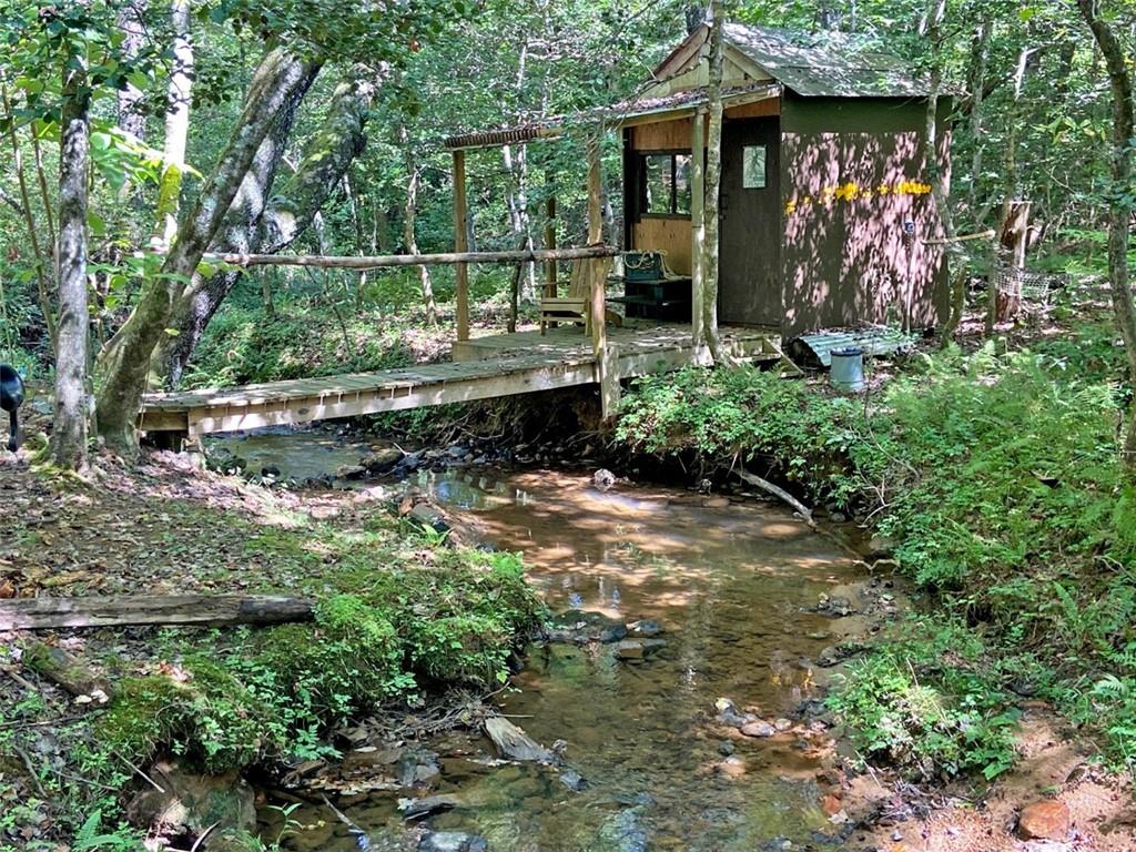 A CREEK RUNS THROUGH IT...Yep, right down the middle of this 4.3 acre parcel (two lots) outside of Blue Ridge, GA. And pretty waters they are too, crystalline clear and chortling gently through fern-lined woodlands. A footbridge takes you across the creek to a cute little garden building with a porch just begging for a rocking chair from which to sit and look at the flowing waters. It's very lovely and quiet here - maybe a few birds, the sound of the water, your own thoughts.
Much of the terrain is perfectly flat or gently rolling, yet the property still has the feel of the mountains with beautiful timber and a native understory. A little branch comes through the side of the property and spills into the creek.
The property comes with a brand-new three-bedroom septic system installed and a cut-in for a basement, or use it for parking. A driveway has been freshly graveled and a bit of clearing has been done.
The scenic town of Blue Ridge is a short drive away, along with all the natural amenities the Mountains have to offer. This one is choice for either a permanent home or a weekend retreat and you'll find this to be one of the prettiest little tracts you're ever likely to come across.