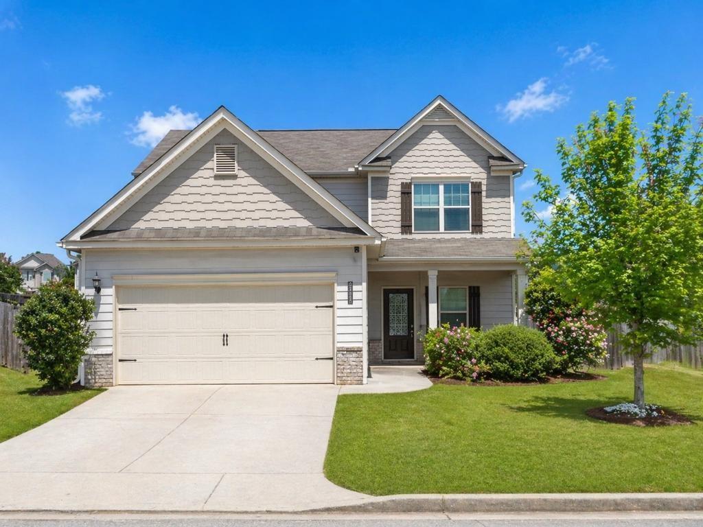 Two-story residential exterior featuring mixed siding, a two-car garage, covered entry porch, and a landscaped front yard with mature plantings