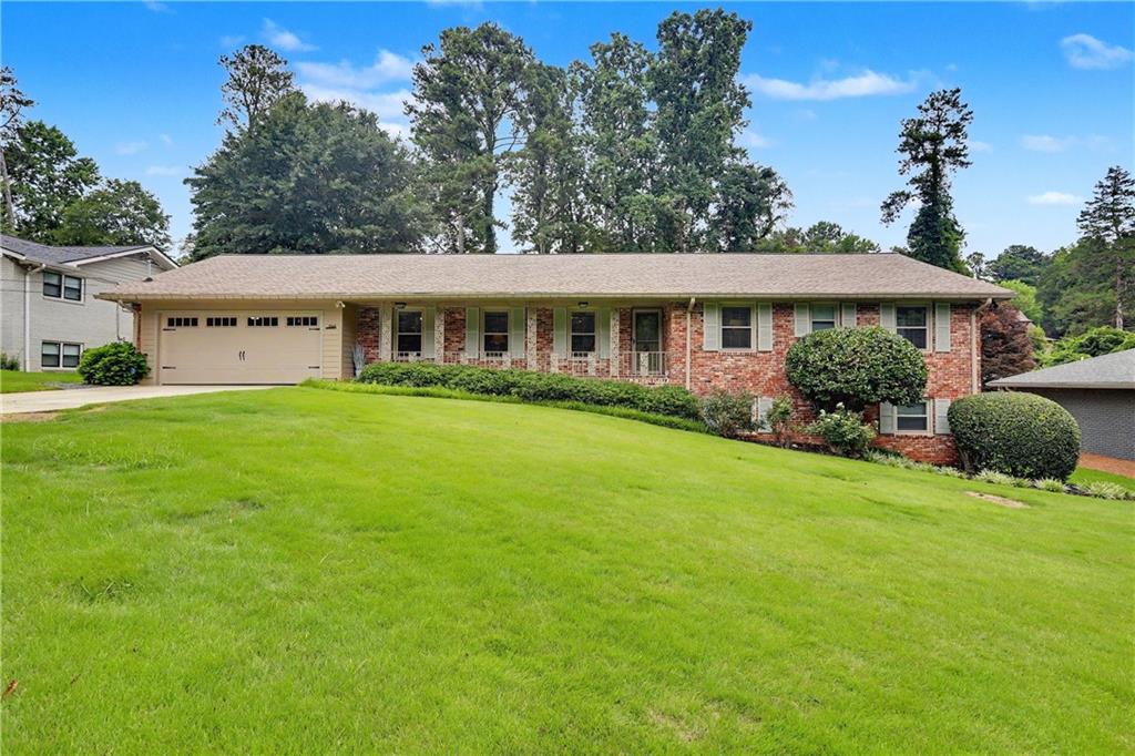 Traditional brick residence featuring a two-car garage, established landscaping, and a sloped front lawn