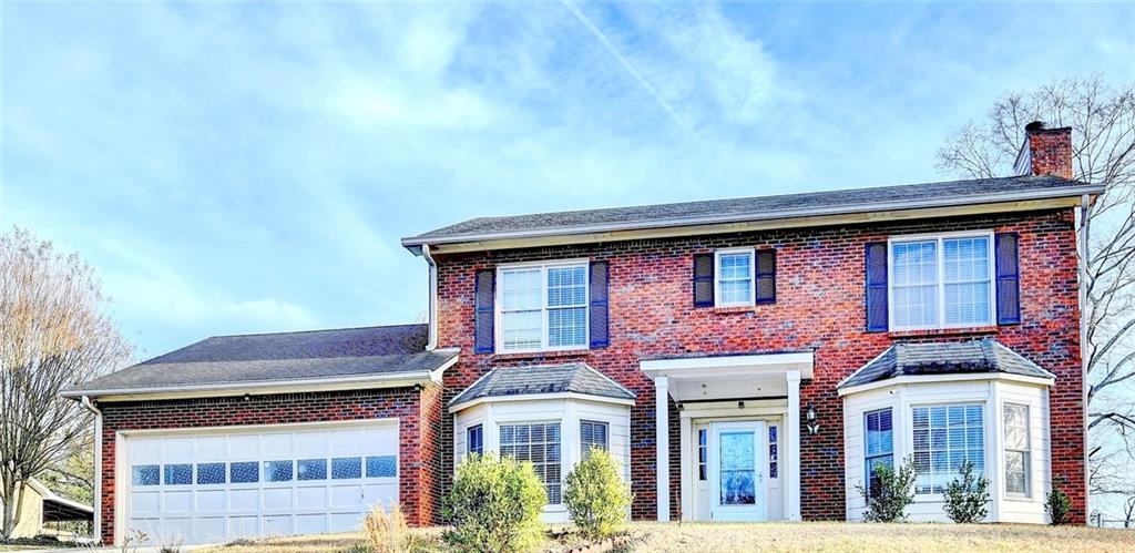 Traditional brick residence featuring a two-story design, an integrated two-car garage with transom windows, and multiple bay window extensions