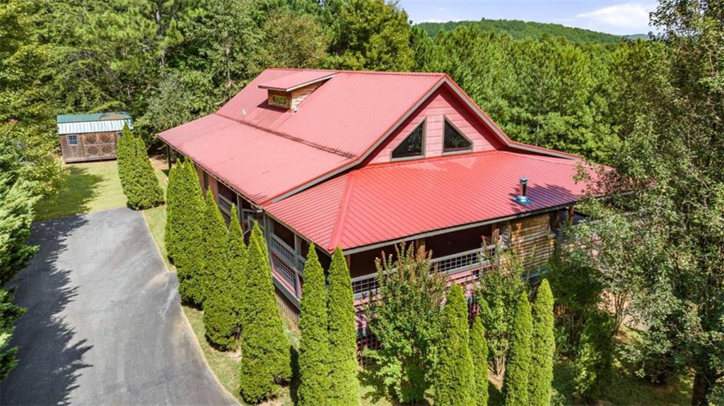 Discover your tranquil retreat in this breathtaking cabin, nestled on a stunning 5.08-acre parcel with the added benefit of no state income tax! Ideal for large families or those who love to entertain, this newly updated home ensures both privacy and comfort in a picturesque setting. As you enter, the inviting great room greets you with its soaring cathedral ceilings and a charming corner fireplace, creating a warm and welcoming atmosphere for gatherings. The heart of this home, the gourmet kitchen, overlooks the great room and features top-of-the-line appliances, including a Viking stove, perfect for culinary enthusiasts. On the main level, you'll find two spacious bedrooms and a versatile additional room that can serve as a butler's pantry or home office, offering flexibility to suit your lifestyle. The expansive primary en suite is a true highlight, boasting a luxurious bathroom complete with an oversized shower and exquisite tile work, along with its own private covered porch-your perfect retreat to unwind. For added convenience, the home includes laundry facilities on all three levels. On the main level, experience the charm of the wrap-around porch with an oversized fireplace-perfect for cozy evenings! Ascend to the upper level to discover another stunning en suite that offers a spa-like experience, complete with its own private deck, providing a serene spot to enjoy morning coffee surrounded by nature. The lower level expands the living space further, featuring a full kitchen, ample bonus/family room, a full bath, and a fourth bedroom, making it perfect for guests or extended family stays. Step outside to enjoy the fully fenced yard, ideal for pets and outdoor activities, complemented by a separate workshop area for your projects. The property offers all paved access and a gated driveway leading to a detached three-car garage, ensuring convenience and security. Enjoy convenient access to Chattanooga, Murphy, and Blue Ridge!