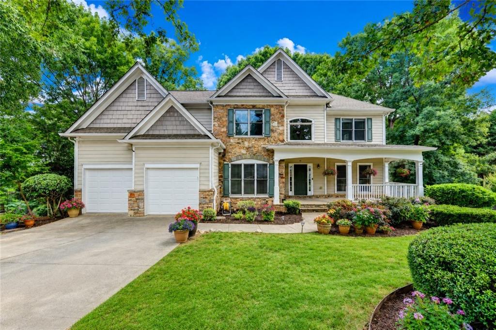 Stately residence featuring a stone and siding facade, covered front porch with white railings, and a two-car garage