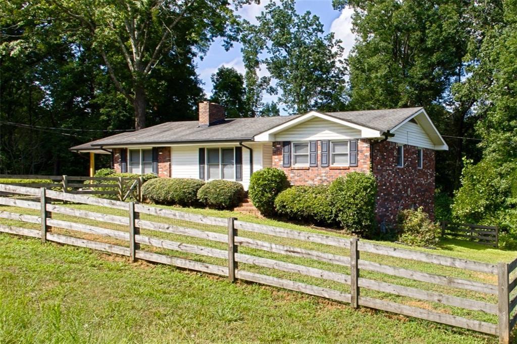 Welcome to your charming farmhouse retreat in Cumming! This desirable 3-bedroom, 2-bath ranch-style home is nestled on a picturesque 1.5-acre corner lot, offering both privacy and timeless charm. From the moment you arrive, you’ll appreciate the inviting fenced front yard and the serene, wooded backyard—perfect for children, pets, and relaxing afternoons. Inside, you’ll find beautiful real hardwood floors, fresh paint throughout, and stylish shiplap accent walls that add warmth and character to every room. The heart of the home centers around a true masonry fireplace, ideal for cozy evenings. The kitchen comes equipped with essential appliances including a refrigerator, dishwasher, electric cooktop, and electric oven. The open-concept layout flows seamlessly to a spacious living area and out to a large entertainment deck—perfect for hosting summer barbecues or enjoying your morning coffee in peace. Downstairs, a full unfinished basement offers incredible potential with a workshop area and a wood stove—ready for your vision to transform it into additional living space, a home gym, or even an in-law suite. Blending rustic charm with tasteful updates, this home is a rare find in a peaceful, private setting—just minutes from all the conveniences and attractions that Cumming has to offer.