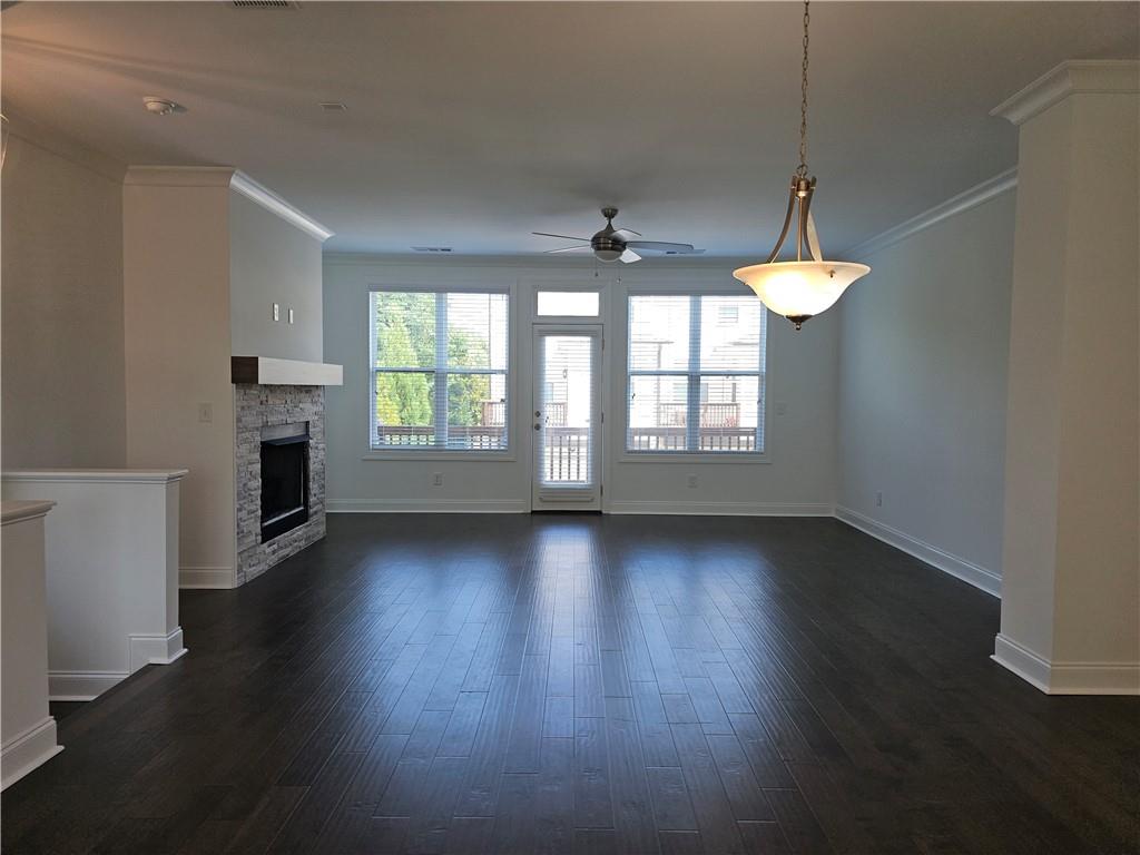 Expansive interior featuring dark wood-finish flooring, a stone-front fireplace with a wood mantel, and crown molding