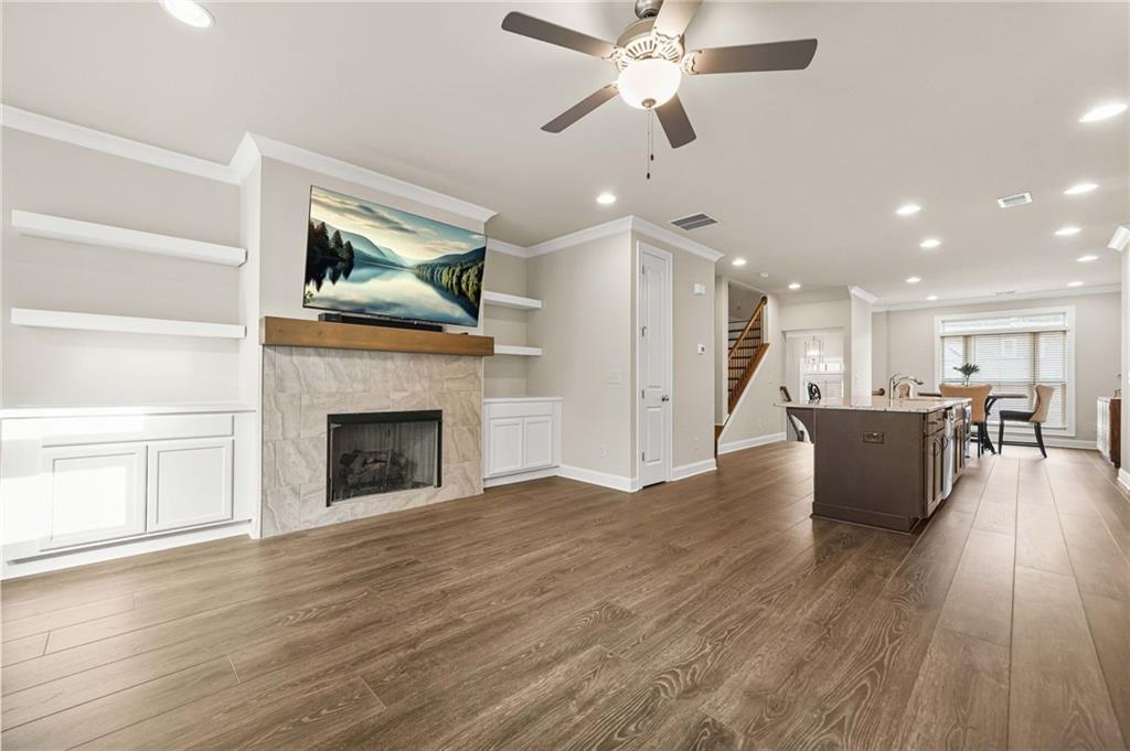 Living room with crown molding, dark wood-type flooring, a fireplace, recessed lighting, and stairs