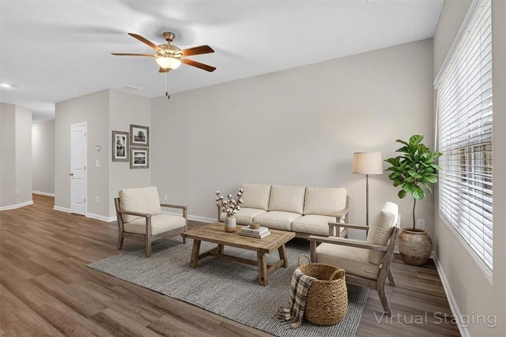 Spacious living area featuring wood-finish flooring, neutral wall tones, and a ceiling fan with integrated lighting