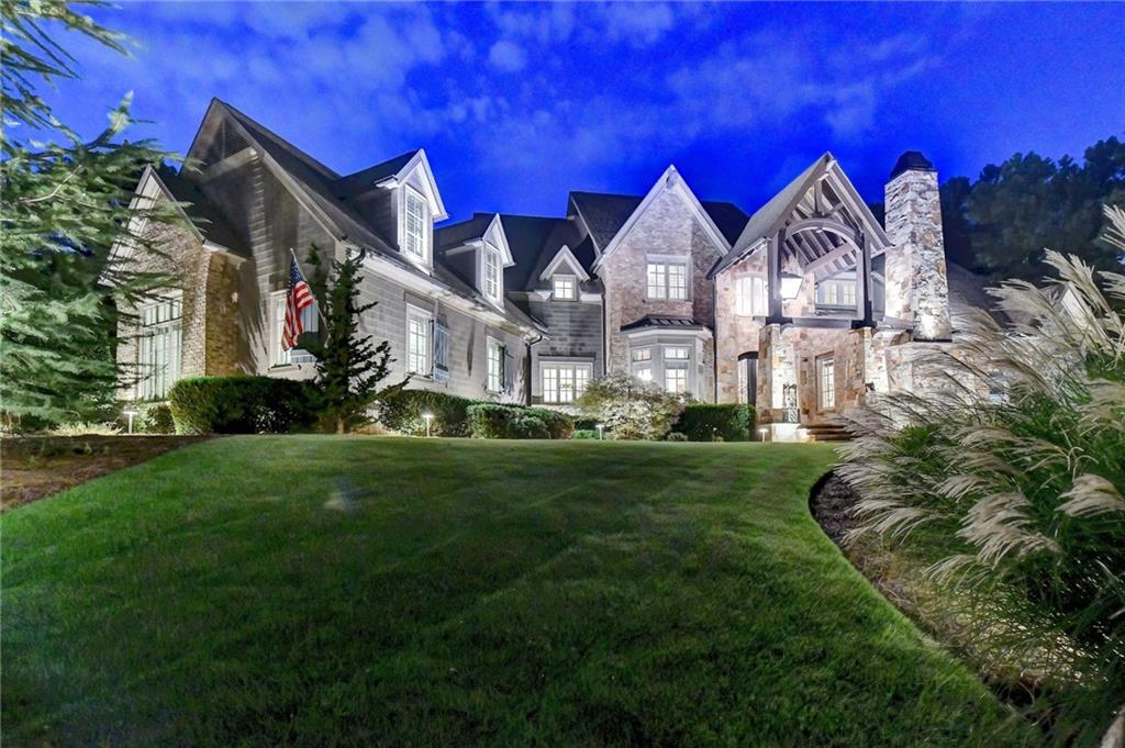 Welcome to this exceptional River Club estate, perfectly positioned between the 5th AND 6TH HOLES of the prestigious Greg Norman GOLF COURSE. This custom-built masterpiece features 5 bedrooms, 6 full and 3 half baths, a MASTER-ON-MAIN, WALK-OUT HEATED SALTWATER POOL, and a finished TERRACE LEVEL —all crafted with meticulous attention to quality and design. Step through the grand stone porch into a foyer flanked by a sophisticated OFFICE with MARBLE FIREPLACE and a DINING ROOM with bay windows and beamed ceilings. The soaring FAMILY ROOM boasts RECLAIMED WOOD BEAMS, a floor-to-ceiling stone fireplace, and views of the POOL and outdoor living spaces. The gourmet kitchen features brick accents, high-end cabinetry, Stainless steel WOLF /SUB-ZERO APPLIANCES, granite island, walk-in pantry, and a wet bar. A sunny BREAKFAST ROOM opens to the COVERED STONE PORCH with FIREPLACE, built-in GRILL, fridge, and full pool bath, ideal for entertaining. The luxurious MAIN FLOOR owner’s suite includes a BEAMED tray ceiling, FIREPLACE, bay windows, and spa-like bath with jetted tub, double vanities, walk-through shower, and custom walk-in closet. Additional main-level amenities include a large laundry, mudroom, powder room, and built-in workstation. Upstairs offers a cozy loft, three spacious en-suite bedrooms, a SECOND LAUNDRY, and an unfinished BONUS ROOM. The daylight TERRACE LEVEL is an entertainer’s dream with HANDCRAFTED woodwork, brick and wood-paneled walls, SLATE floors, a BAR, GAME room, GYM, GUEST suite, and powder room. Outside, the rare WALK-OUT Pebble-Tec SALTWATER pool features a waterfall, HOT TUB, FIREPLACE, covered patio, and lush landscaping—just steps from the GOLF COURSE. Top-tier features include a DEEP WATER WELL, Generac WHOLE HOME GENERATOR, WATER FILTRATION & HUMIDIFIER systems, app-controlled LUTRON LIGHTING, extensive outdoor lighting, 4 CAR GARAGE & large motor court. Built from the ground up by the ORIGINAL OWNERS with no expense spared, this home is the pinnacle of luxury in Atlanta’s premier gated golf/swim/tennis community—The River Club.