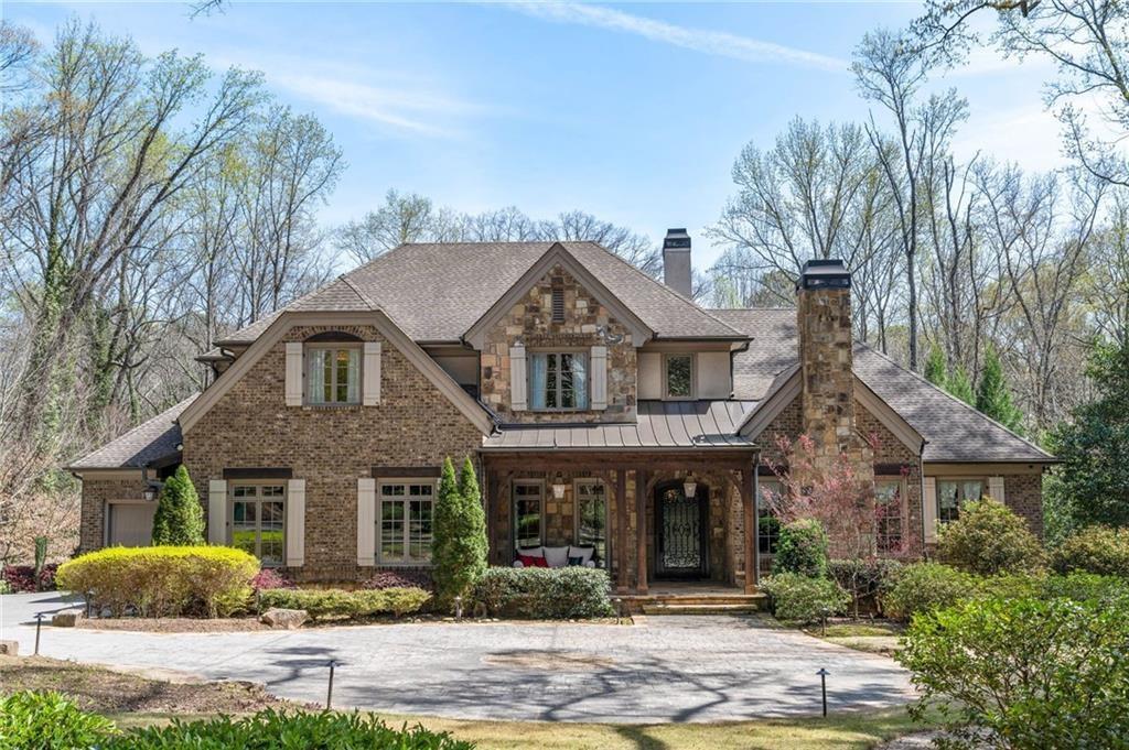 View of front of house featuring covered porch, a chimney, stone siding, a standing seam roof, and driveway