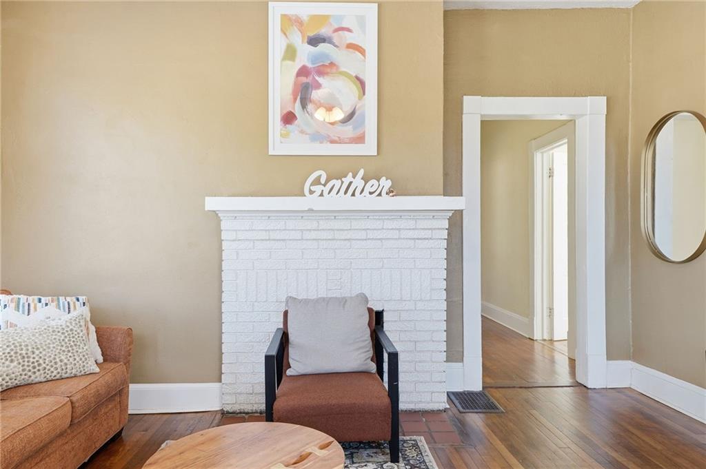 Cozy living room featuring a white brick fireplace with "Gather" sign, an armchair, and a brown sofa, showcasing a warm, inviting atmosphere ideal for family gatherings in a duplex property at 1420 Sylvan Road SW, Atlanta.