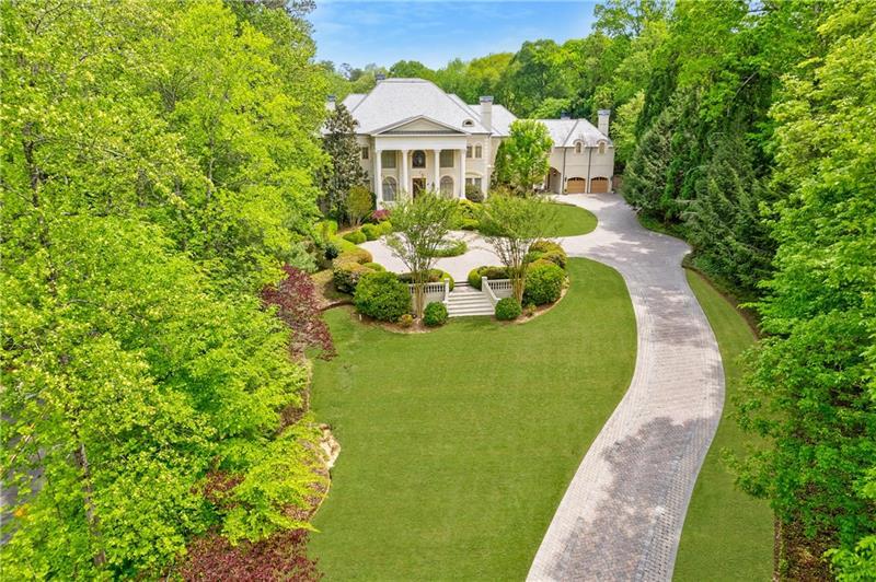 Don't miss this classic beauty, close to everything Metro Atlanta has to offer, yet still secluded and quiet! Situated on a hillside lot among lush greenery and manicured grounds that create the ultimate retreat, 4787 Northside Drive offers a fully equipped guest house, a porte cochere, an elevator and a spectacular outdoor entertainment space that includes a patio area with a pool, an outdoor kitchen, a basketball court and a playground. This private, gated estate in Greek Revival style boasts a full-height entry porch with a pediment supported by Corinthian-style columns welcoming to an interior in which no expense was spared.  Designed to comfortably accommodate large gatherings, the first level is characterized by opulence, resplendent lighting and intricate architectural details in rooms where marble and stone lend gravity to the space. Commencing with a grand bifurcated staircase in the grand foyer, it centers around a banquet-sized dining room with a fireplace and a salon and a formal fireside living room dominated by a wall of windows. Ascend the circular stairs in the home office featuring a fireplace and a TV to find a library with gorgeous built-ins. Off the living room, the kitchen boasts a large center island, a walk-in pantry, plenty of solid-surface countertop prep space, light cabinetry and professional-grade stainless steel appliances (including a Sub-Zero fridge and a double oven). An adjacent keeping room features a coffered ceiling, built-ins, a fireplace and large windows. Discover a spacious retreat in the primary en suite, featuring a sitting area with a fireplace, a show-stopping walk-in closet and a spa-inspired bathroom that includes a walk-in shower, a garden soaking tub and dual vanities. Tray ceilings add a feeling of height. The second level, with an abundance of additional bedrooms each with an en suite bathroom and closet space, offers lavish options for privacy and personalization for everyone. Upper and lower laundry rooms with storage handle all home organization needs with ease.  Fully equipped with a wine cellar, a home theater, a billiard/game room, a bar, a home salon, an exercise room and a sauna, this estate offers every convenience. The guest house offers flexible living arrangements for multigenerational households as well as a place for visitors. The four-car garage provides plenty of accommodation for vehicles and offers space for storage.