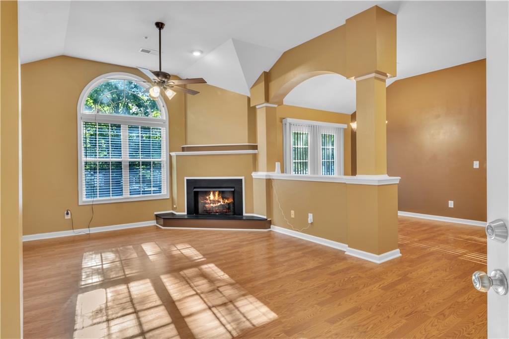 Unfurnished living room with a lit fireplace, light wood-style flooring, vaulted ceiling, ceiling fan, and recessed lighting