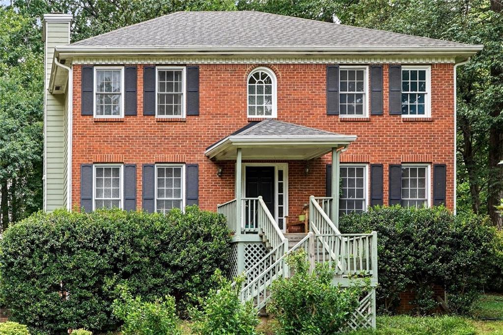 Traditional two-story brick residence with an arched window, dark shutters, and a covered porch entry