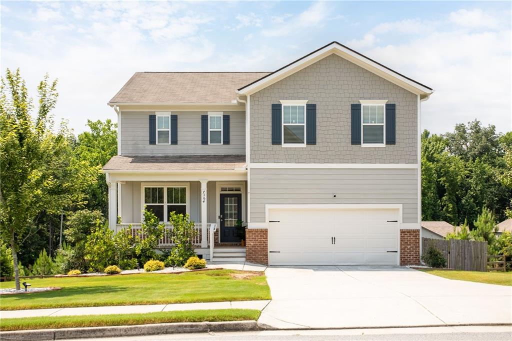 Two-story residence featuring light gray siding, dark shutters, a covered porch with white railing, a two-car garage, and a concrete driveway