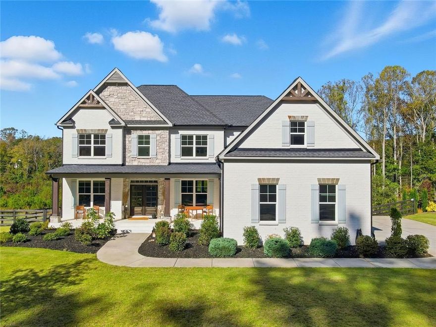 Set within the sought-after Milton Overlook community near Birmingham and Batesville Road, this home combines high-end design with everyday comfort. The exterior blends painted brick and stone for timeless curb appeal, while the inviting front porch hints at the open, light-filled interiors inside. Step into the two-story great room where a wall of soaring windows and a sleek fireplace frame serene, protected green space—no neighbors behind you, just a backdrop of nature and sky. Each evening, the view transforms as the sun sets across the treetops, casting warm light into the room and painting the sky in color. The open layout flows effortlessly into the chef’s kitchen, complete with white craftsman cabinetry, a massive quartz island, stainless-steel appliances, a gas cooktop, and a double oven for effortless entertaining. A butler’s pantry and drop zone help keep life organized, while 10-foot ceilings elevate the dining and library spaces. The main-level guest suite offers privacy and natural light, perfect for visitors or multi-generational living. Upstairs, the oversized primary suite features a sitting area and an expansive custom closet. The spa-style bath invites relaxation with a freestanding soaking tub, walk-in shower, and dual vanities. Three additional bedrooms each include large closets and access to well-appointed baths. The unfinished daylight basement with tall ceilings and full-size windows offers space to expand with a theater, gym, or recreation room. Outdoors, enjoy  terrace level patio and deck overlooking a fenced yard and forever-green views—perfect for morning coffee or sunset evenings by the fire pit. Additional features include a three-car garage with an electric-vehicle charging port, and community amenities such as a pool, tennis courts, and a playground.