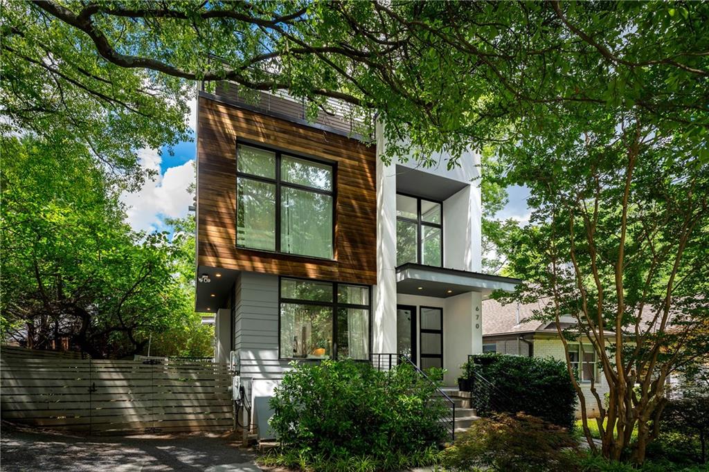 Nestled in the heart of Old Fourth Ward, on one of the quietest and most idyllic streets in the neighborhood, but just moments from the Atlanta BeltLine, Old Fourth Ward Park, Ponce City Market, and Krog Street Market, this striking modern residence, designed by the prolific architect Jordache Avery of XMetrical, offers the rare opportunity to enjoy sophisticated city living amid a lush urban canopy. A bold architectural statement, the exterior marries hardcoat masonry stucco with richly toned Brazilian hardwood, creating a refined yet organic presence. Inside, soaring ceilings and expansive windows bathe the interiors in natural light, framing tranquil treetop views and enhancing the home’s warm modernity. The central great room is anchored by a sleek linear fireplace and flanked by walls of glass, establishing a seamless connection between indoors and out. The designer kitchen features quartz countertops, custom contemporary cabinetry, and a suite of professional-grade stainless appliances. A casual dining area opens through sliding glass doors to a rear deck, ideal for morning coffee or evening cocktails. A beautifully appointed powder room completes the main level. Ascend the dramatic stairwell, an architectural feature in itself, with custom iron balustrades to the private owner’s level. Here, the sun-drenched primary suite offers a quiet retreat, complemented by a spa-inspired bath with dual modern vanities and a wet room complete with dual shower heads and a freestanding soaking tub beneath a tile-clad accent wall. A second ensuite bedroom completes this level. The top floor presents a flexible open-concept lounge, an additional bedroom and full bath, perfect for a home office or guest suite, plus access to a sprawling rooftop terrace. Designed for year-round entertaining, this terrace includes both covered and uncovered areas with generous space for dining and multiple seating areas beneath the stars. The fully finished terrace level offers even more versatility, with a second living room, fourth bedroom, full bath, and abundant room for recreation or media. For added energy efficiency, the residence is equipped with roof-mounted solar panels, further enhancing its modern sustainability. Additional highlights include off-street parking and a Tesla charger. A rare combination of form, function, and location, this is intown living at its finest.